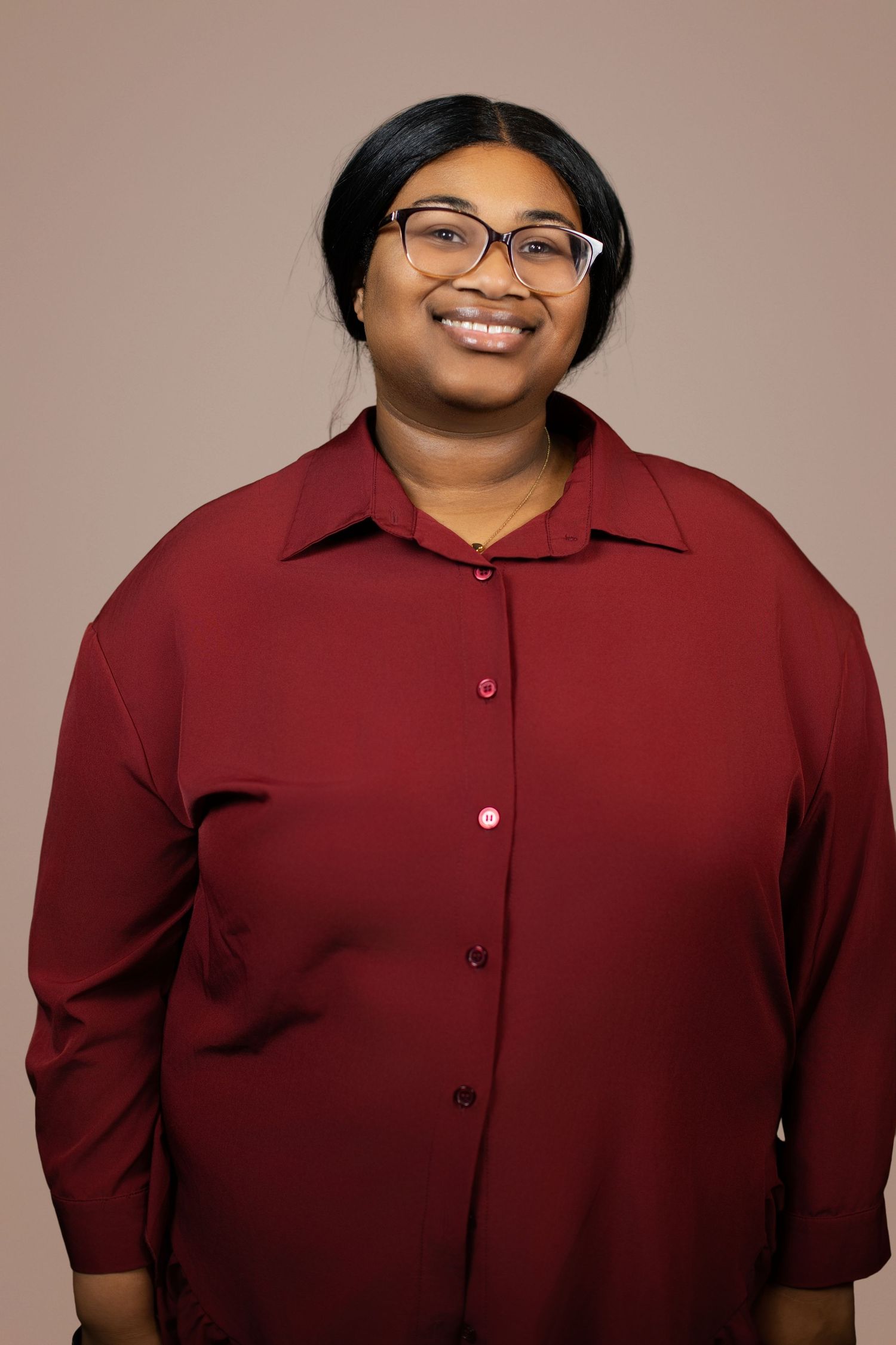 Smiling woman wearing glasses and a burgundy button-up shirt poses for a professional portrait photo.