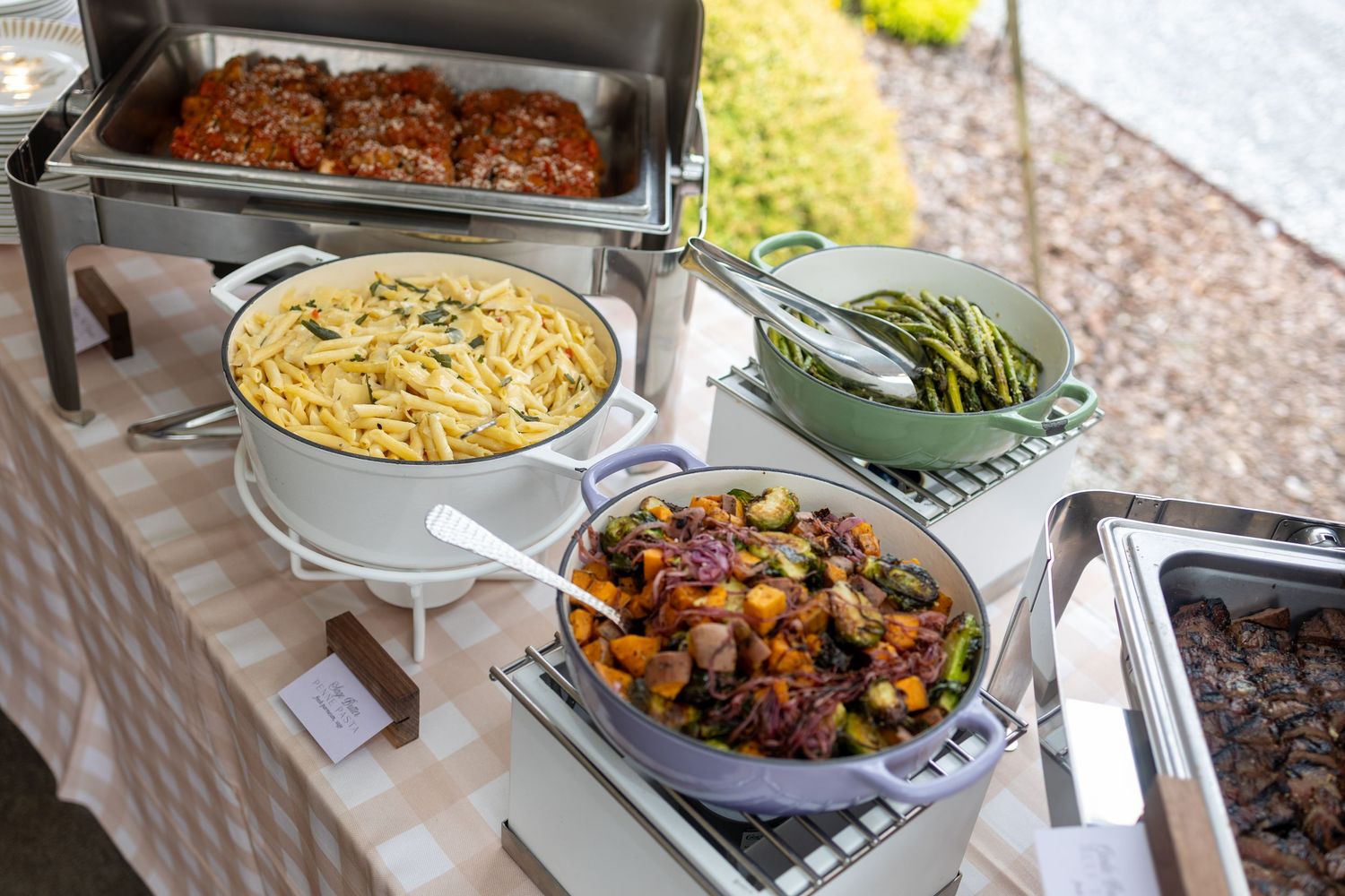 A buffet line displays various hot dishes including pasta, rice, and colorful vegetables in stainless steel serving trays.