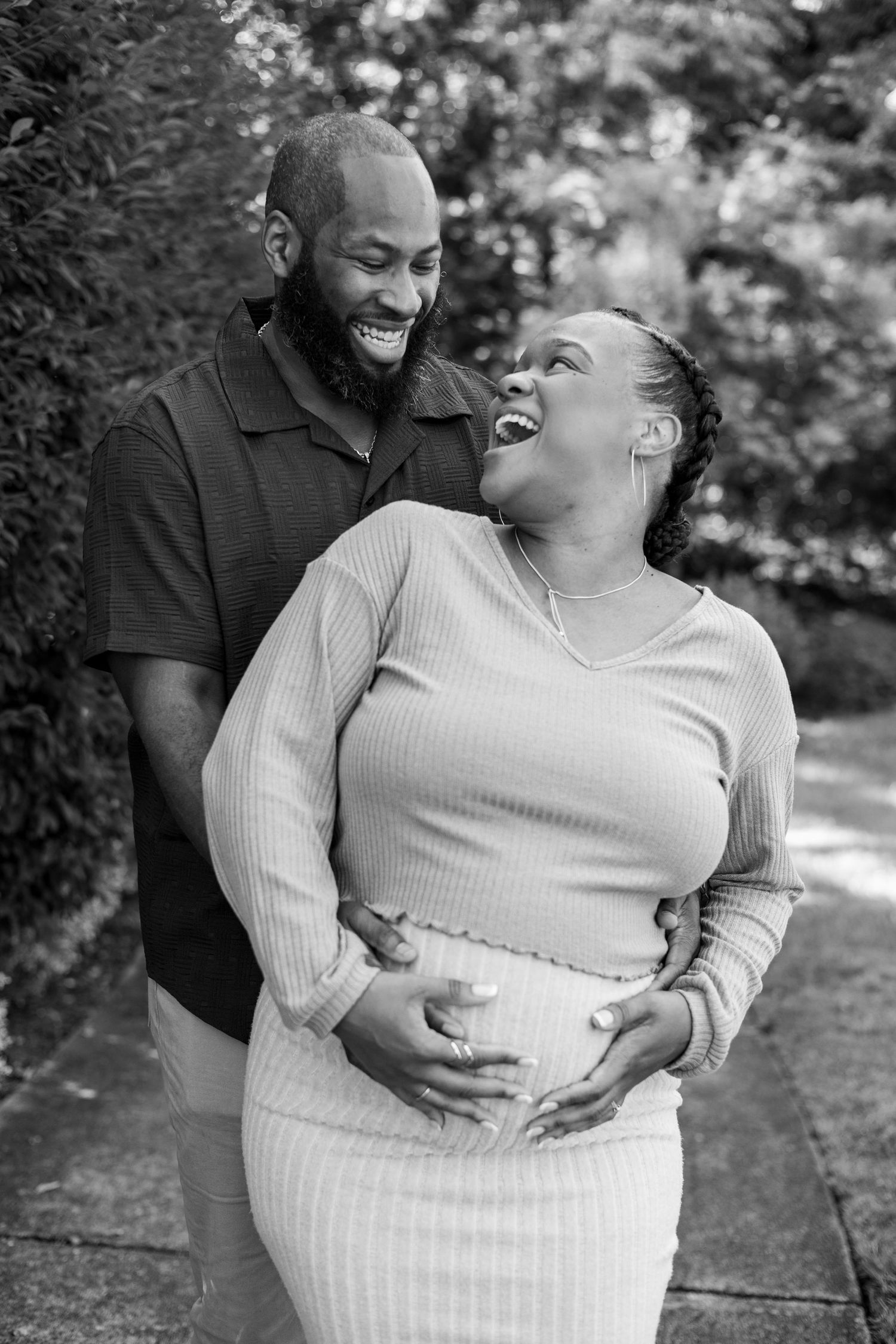 A couple shares a joyful moment while posing together outdoors in black and white.