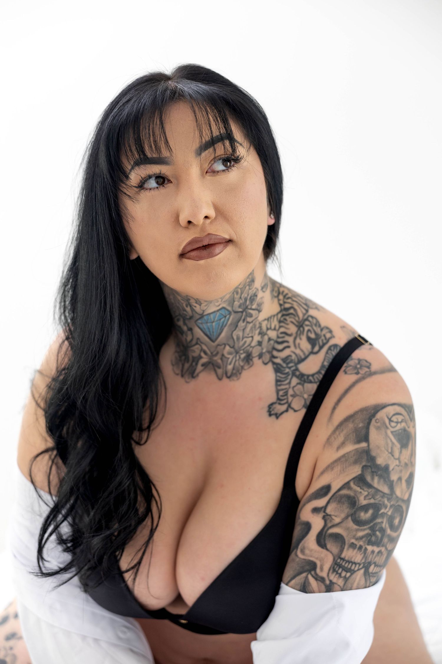 Close up portrait showing intricate neck and arm tattoos against minimalist white background.