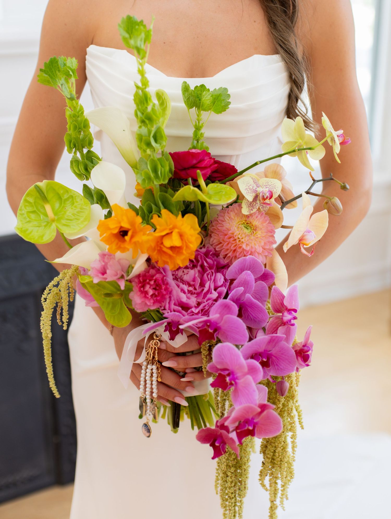 Bride in white strapless gown holding vibrant tropical wedding bouquet with orchids, peonies, anthurium, and amaranthus.