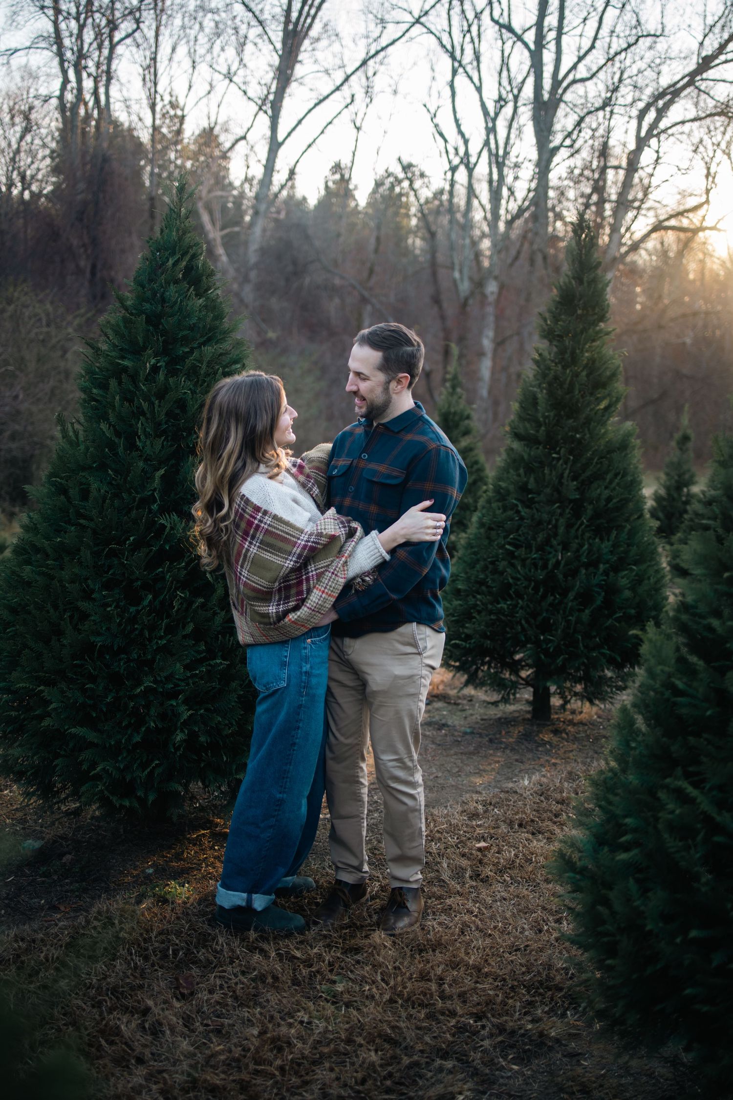 A couple shares a joyful moment while shopping for Christmas trees at a tree farm during sunset.