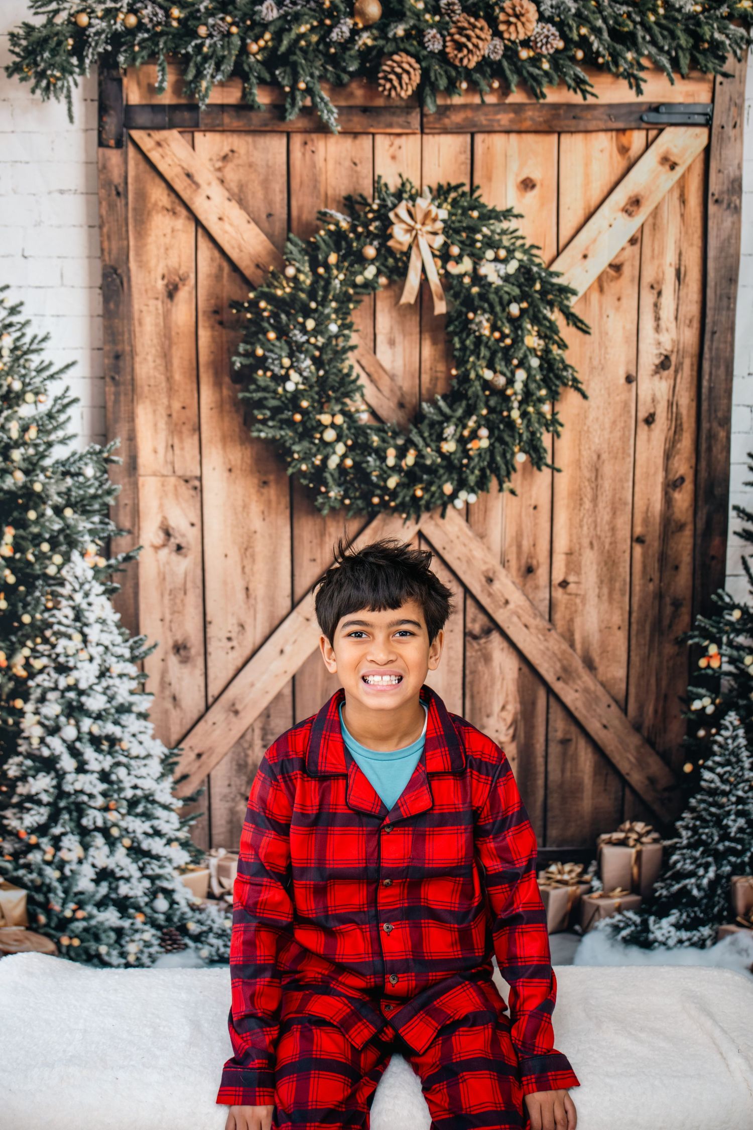 A cozy winter scene with a red buffalo plaid flannel against a rustic wooden barn door with evergreen wreaths and snow.