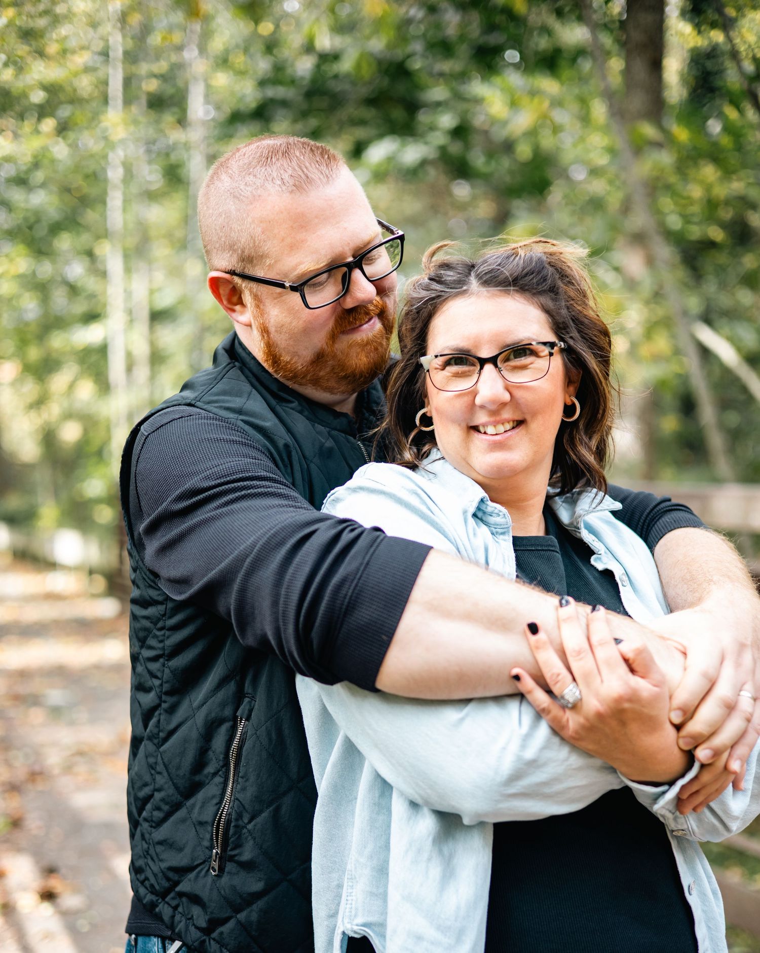 A couple embraces while sharing a joyful moment together in an outdoor setting with trees in the background.