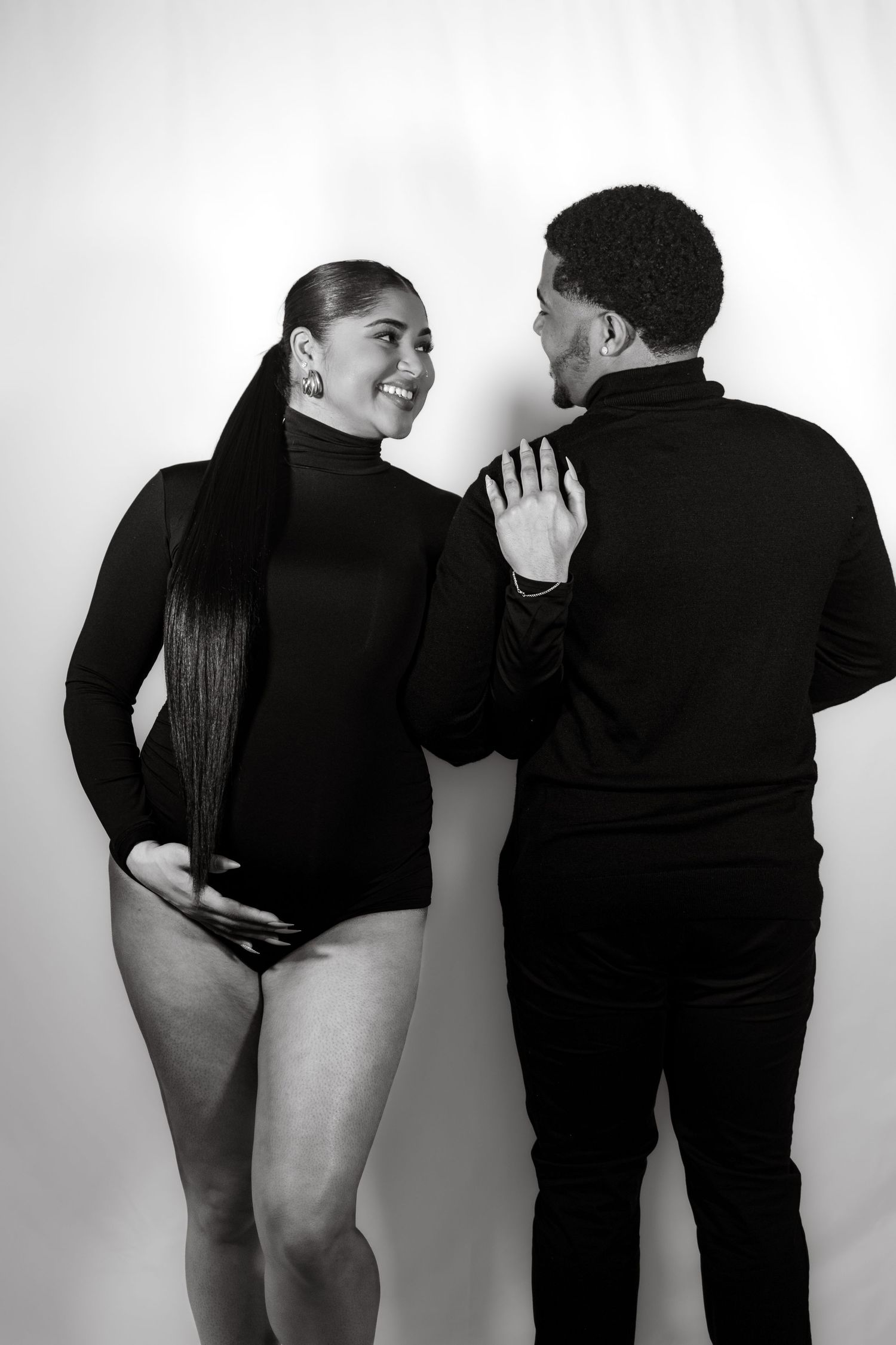 Playful maternity photo series showing couple interacting and laughing in black outfits against white backdrop.