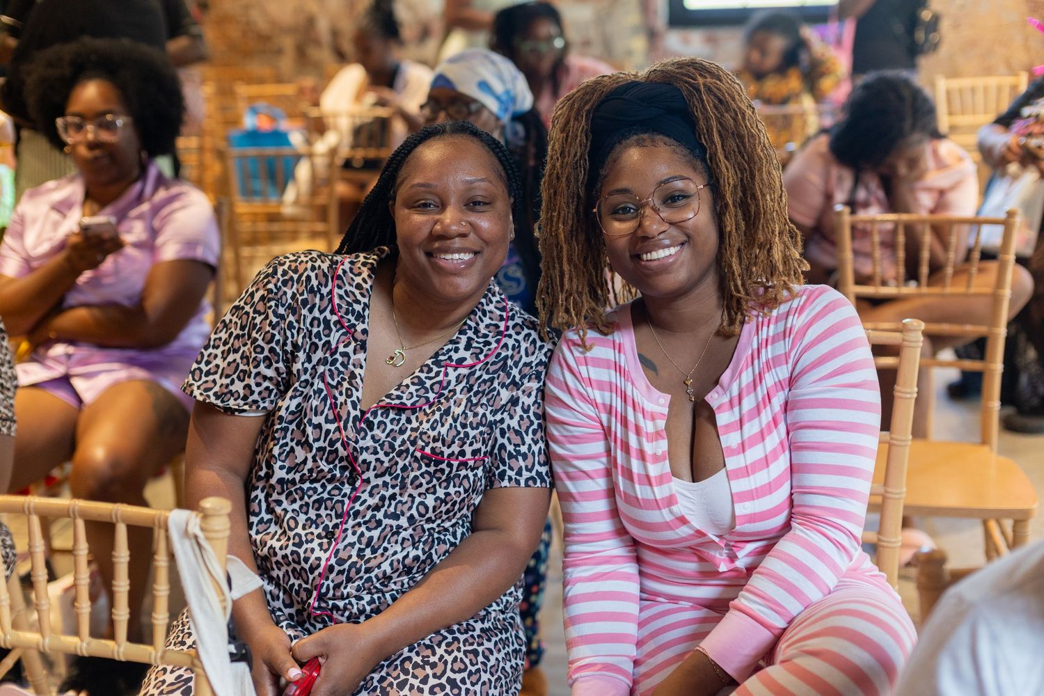 Two smiling women pose together at an indoor event, wearing colorful outfits in a decorated venue.