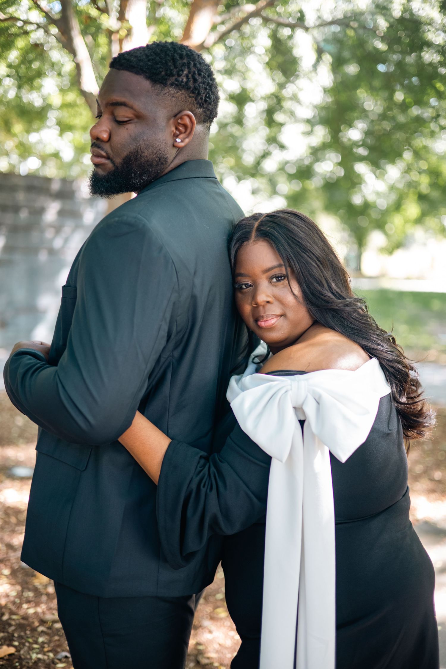 A couple in formal black and white attire embracing outdoors in a romantic photoshoot series.