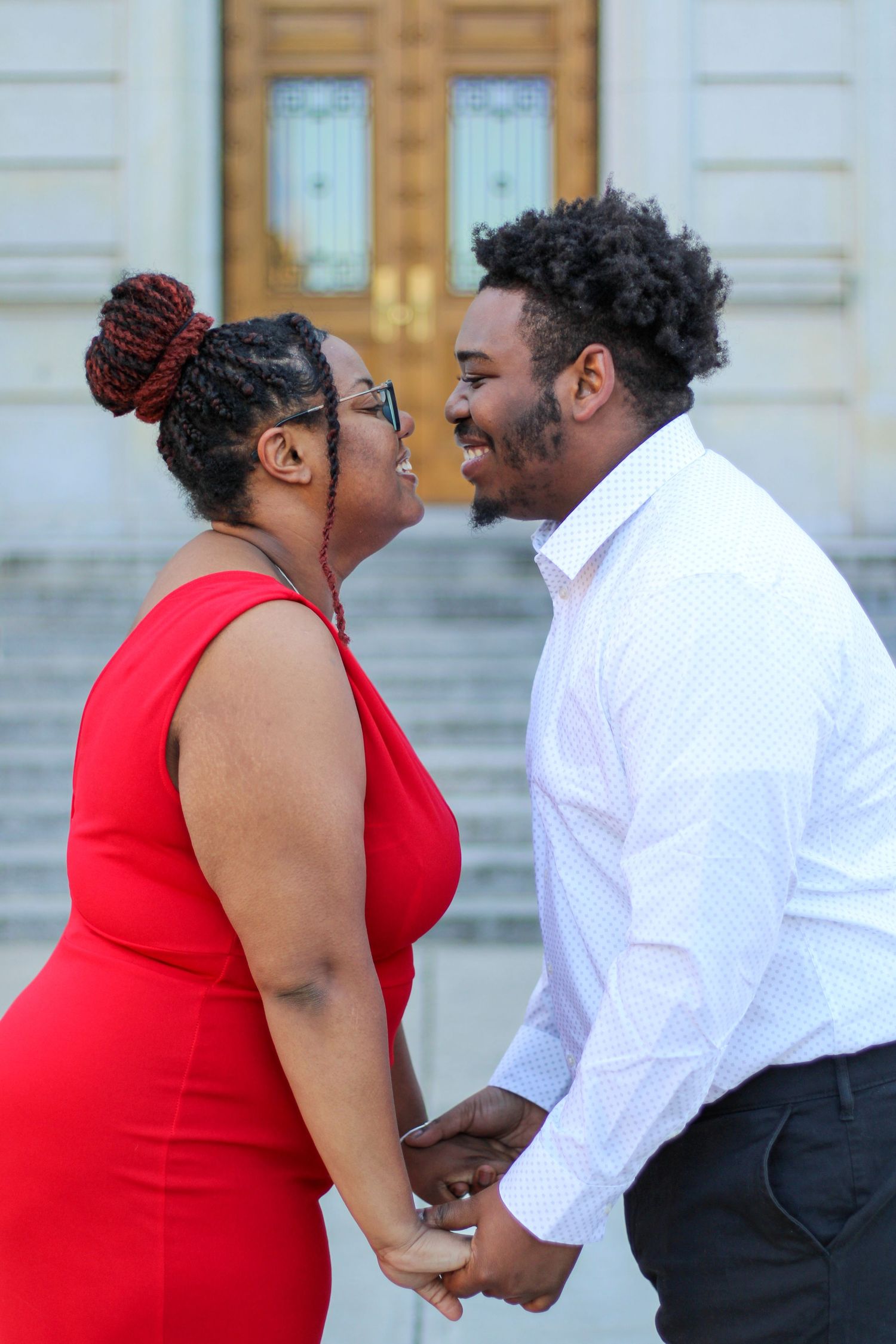 A loving couple shares a close moment on stone steps while dressed in formal red and white attire.