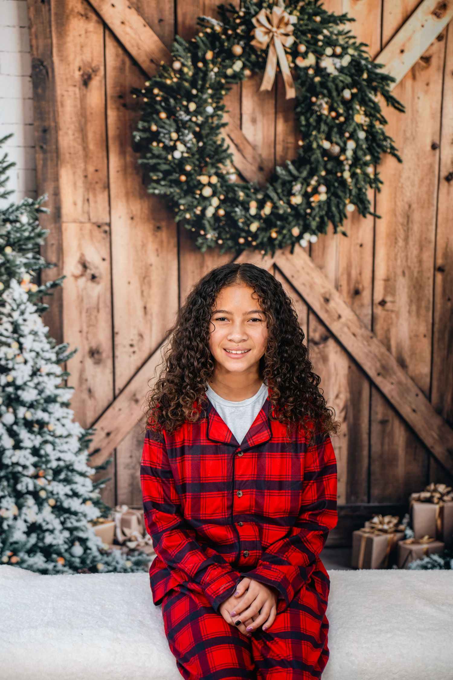 Winter portrait with red plaid flannel against rustic wood backdrop and holiday wreaths in snowy setting.