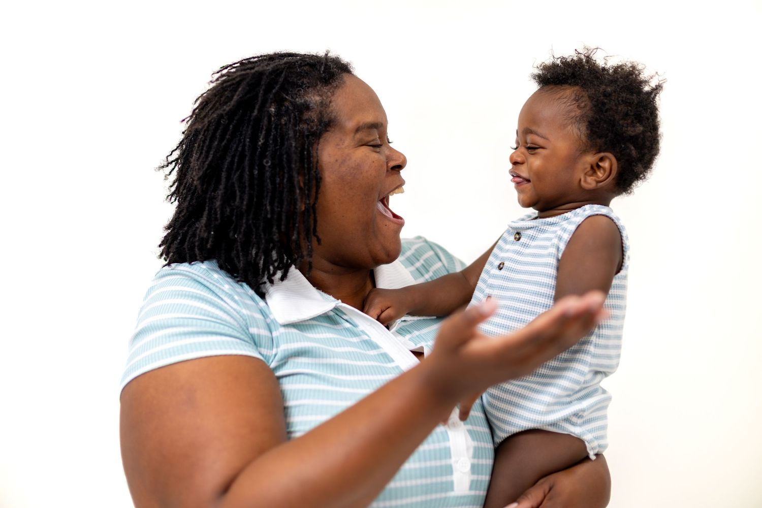 A joyful mother holds her laughing baby, both sharing a playful moment against a white background.