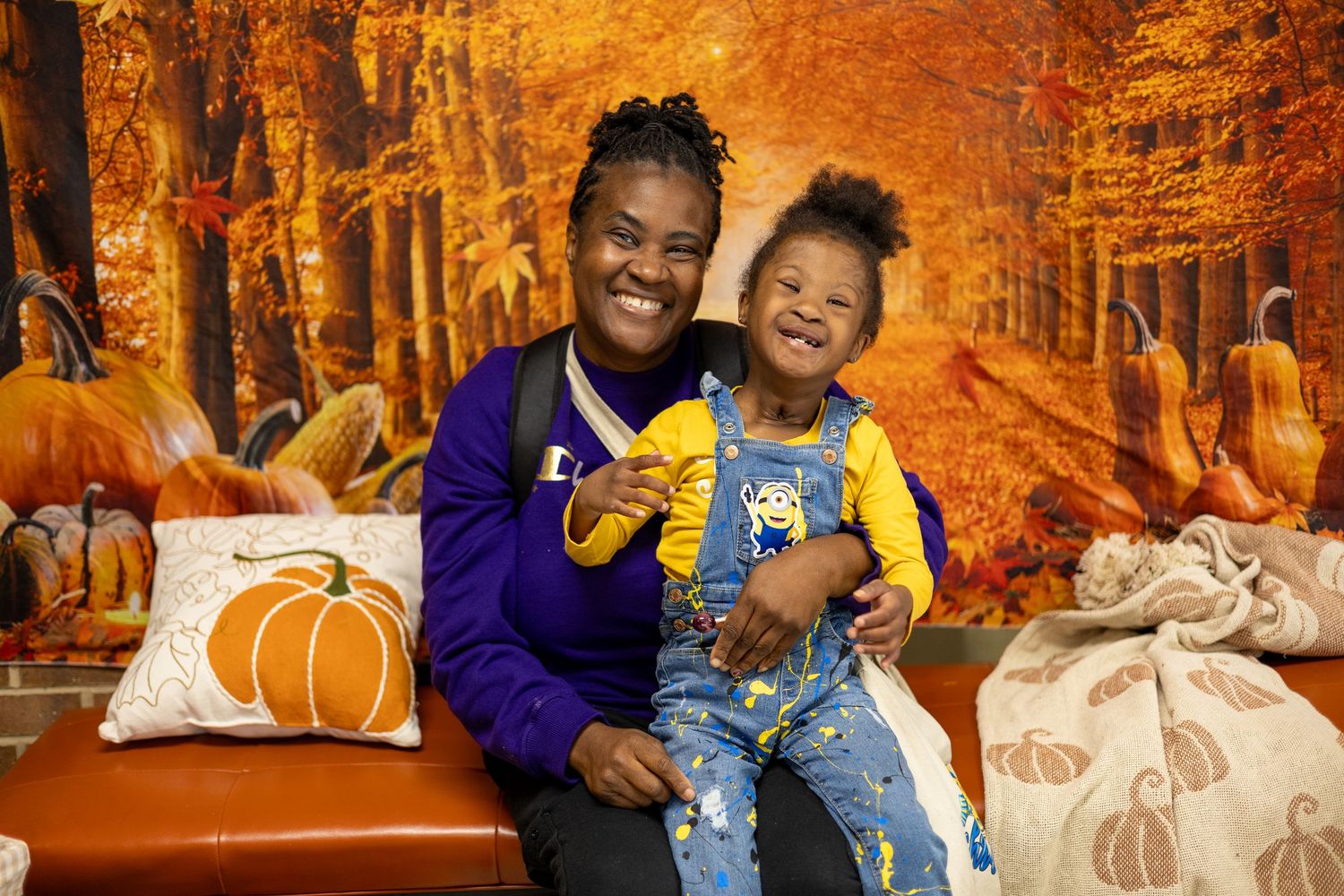 A joyful portrait session featuring decorative pumpkins against a glowing orange autumn forest background.