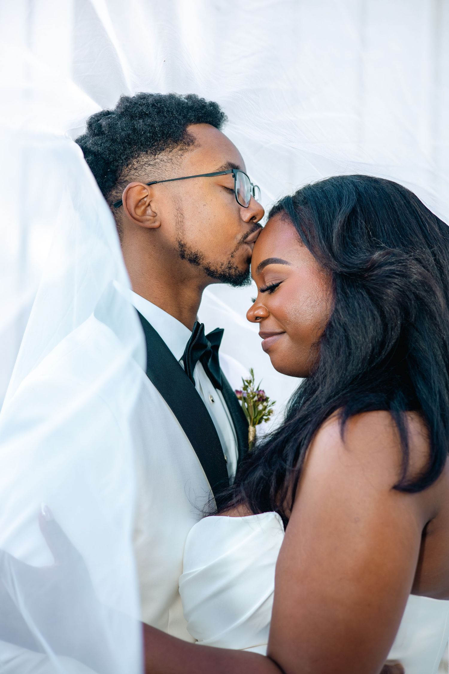 A romantic moment captured between a couple on their wedding day with flowing white curtains in the background.