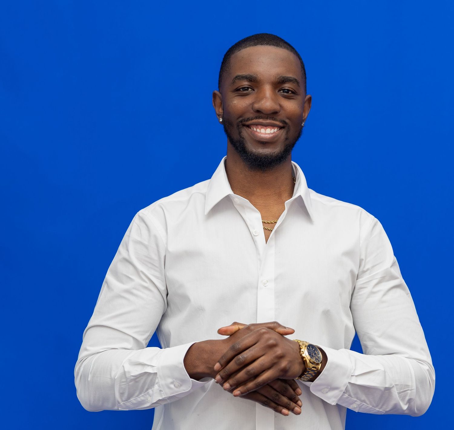 Person in white button-down shirt smiling against blue background in professional headshot series.