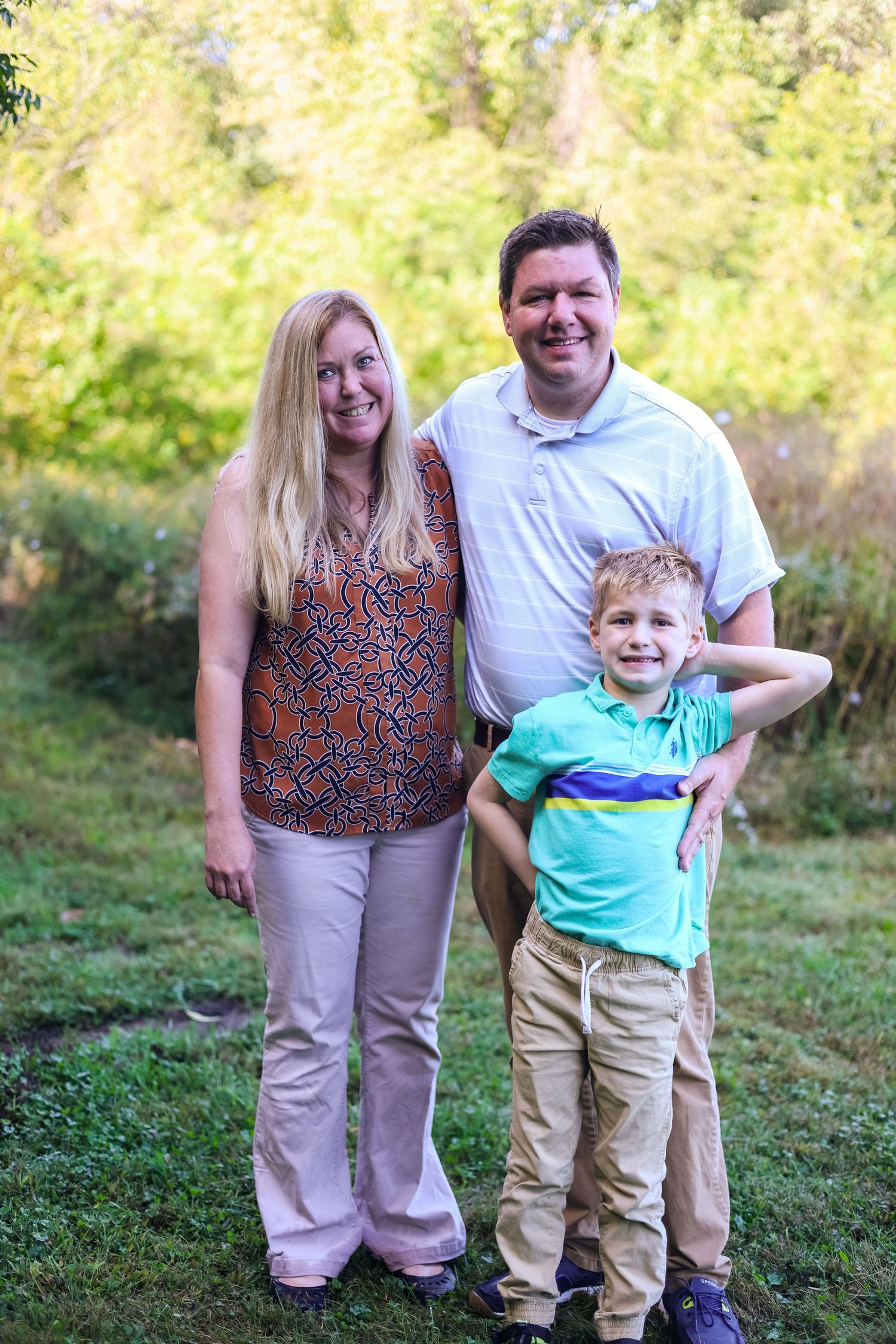 A family poses together outdoors on a grassy hillside during a sunny autumn day.