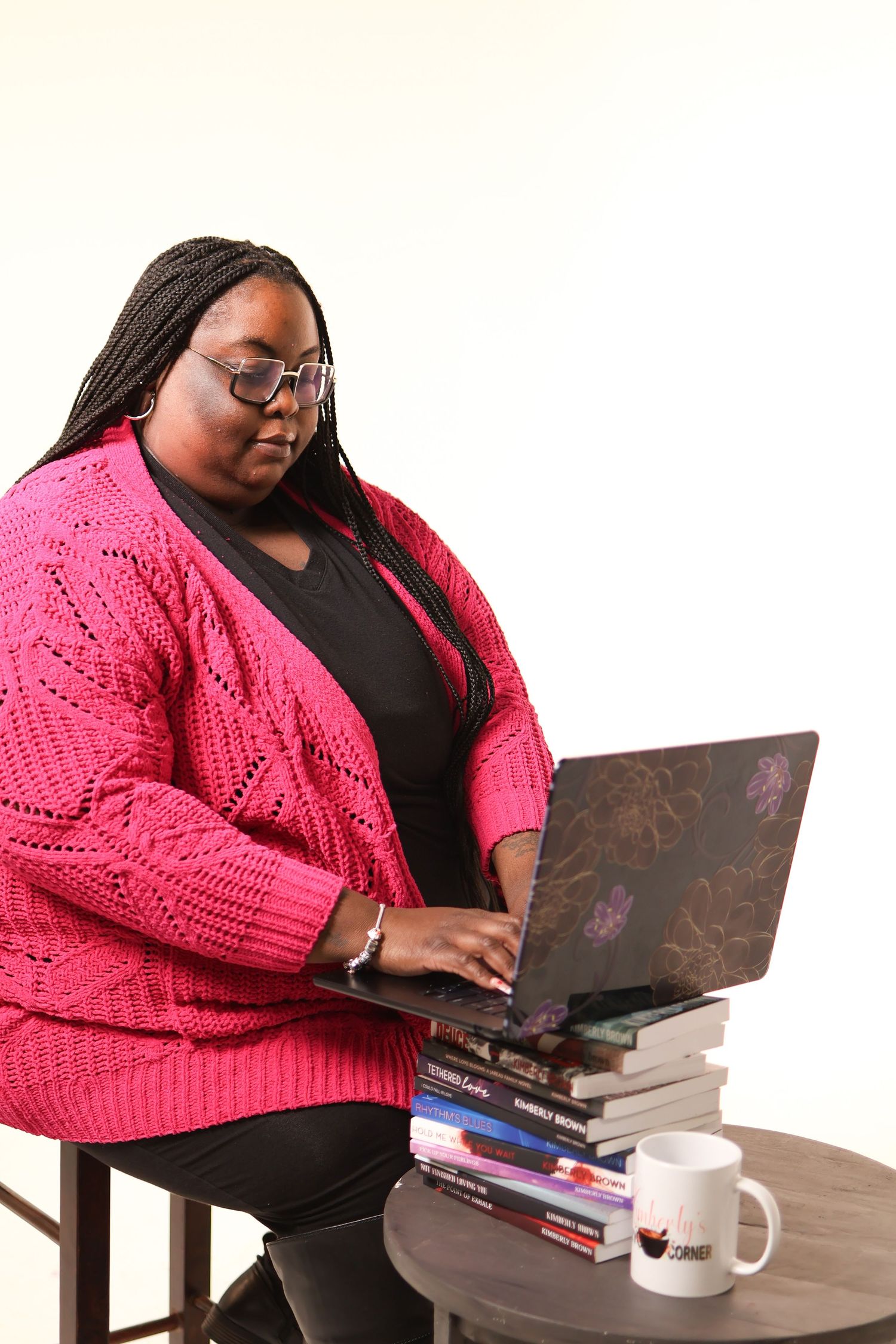 Professional working on laptop at desk wearing pink sweater and black top with coffee mug nearby.