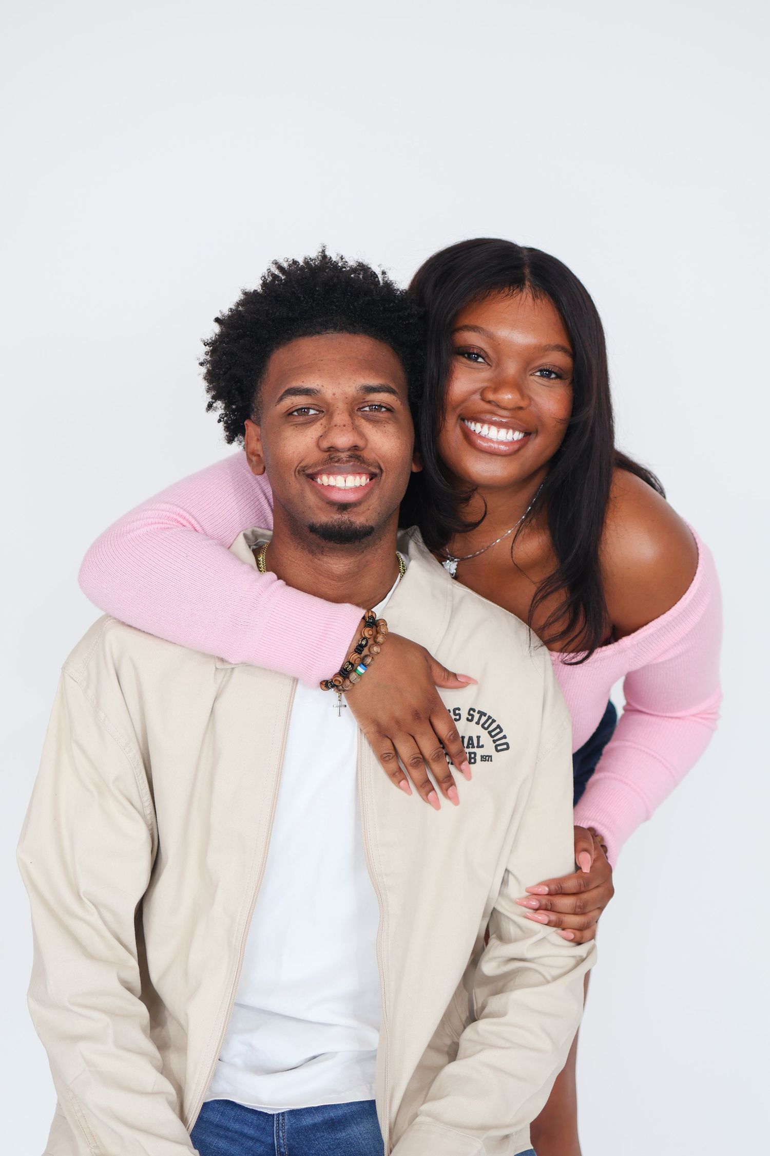 A couple shares a joyful moment together against a white background wearing casual stylish outfits.