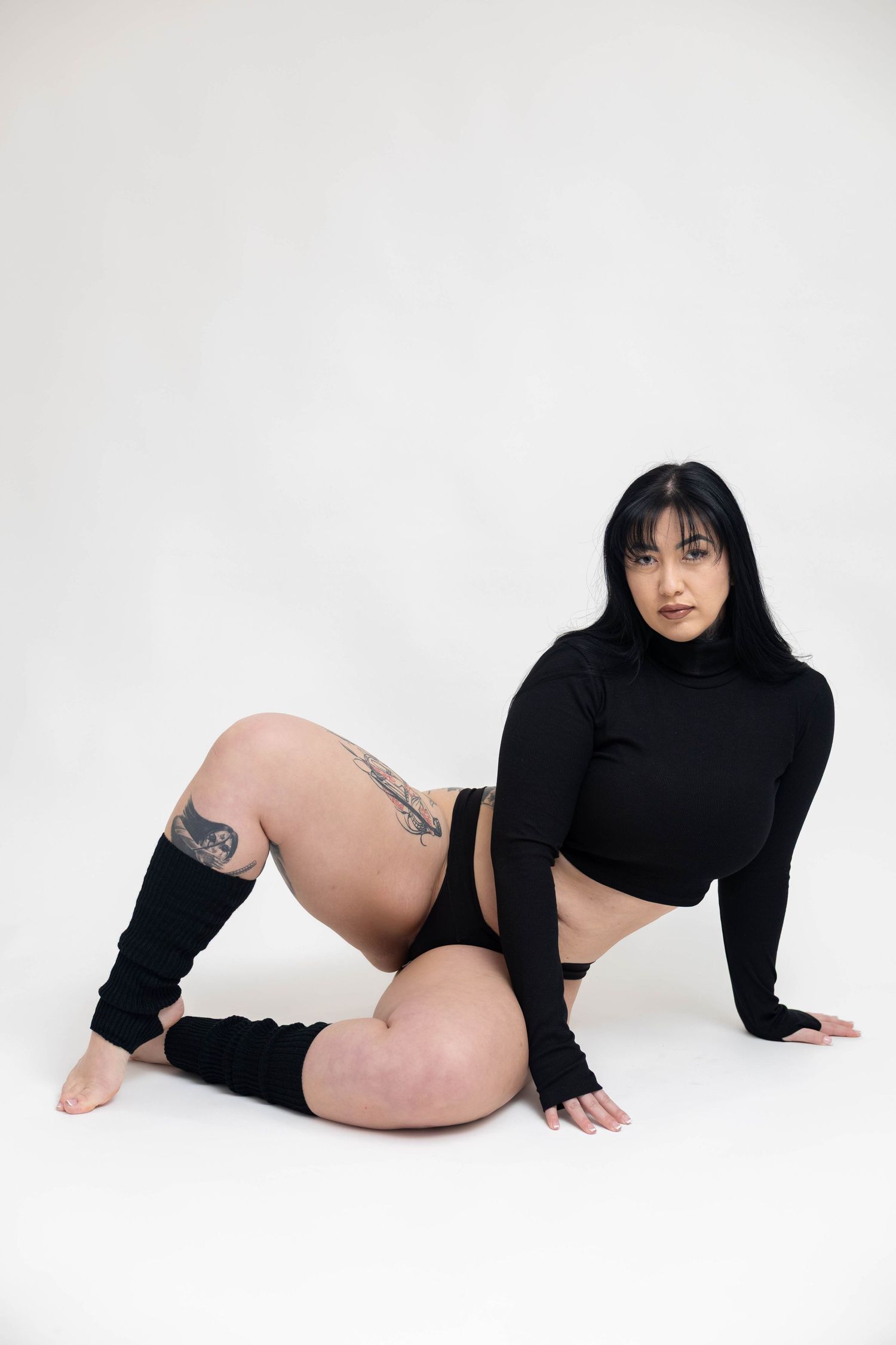 A person in a black long-sleeved top poses artistically on a white backdrop in a minimalist fashion photo series.