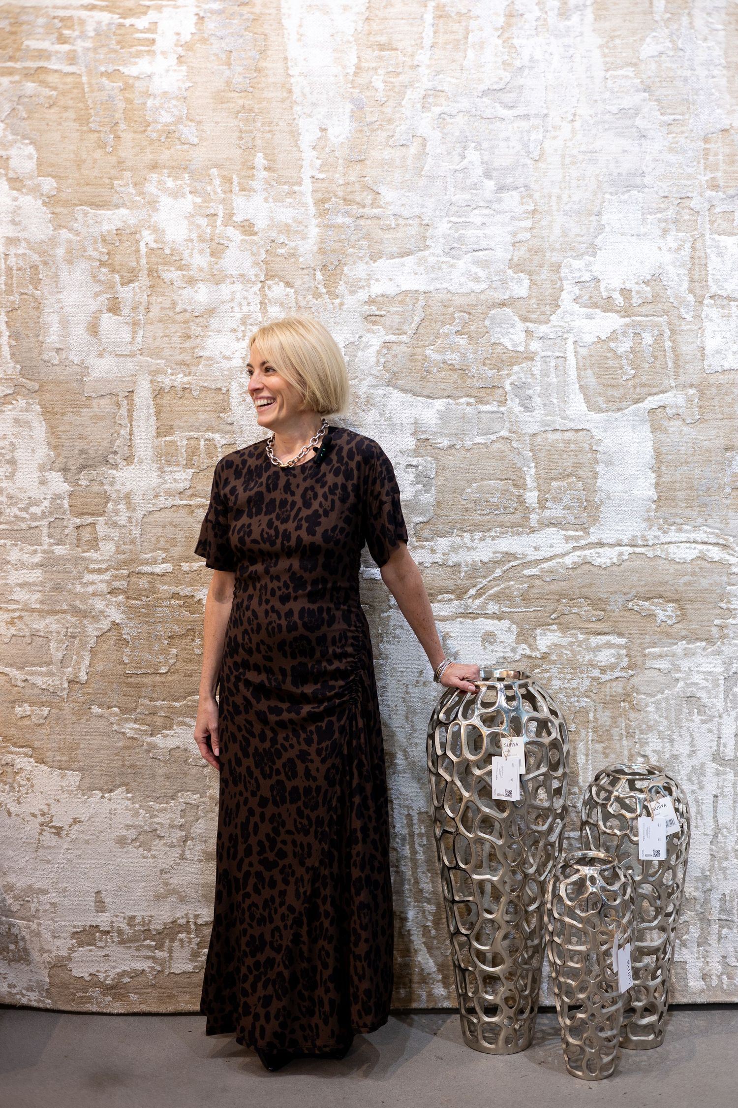 A series of artistic photos showing a dark dress against a textured beige wall with metallic sculptural vases.
