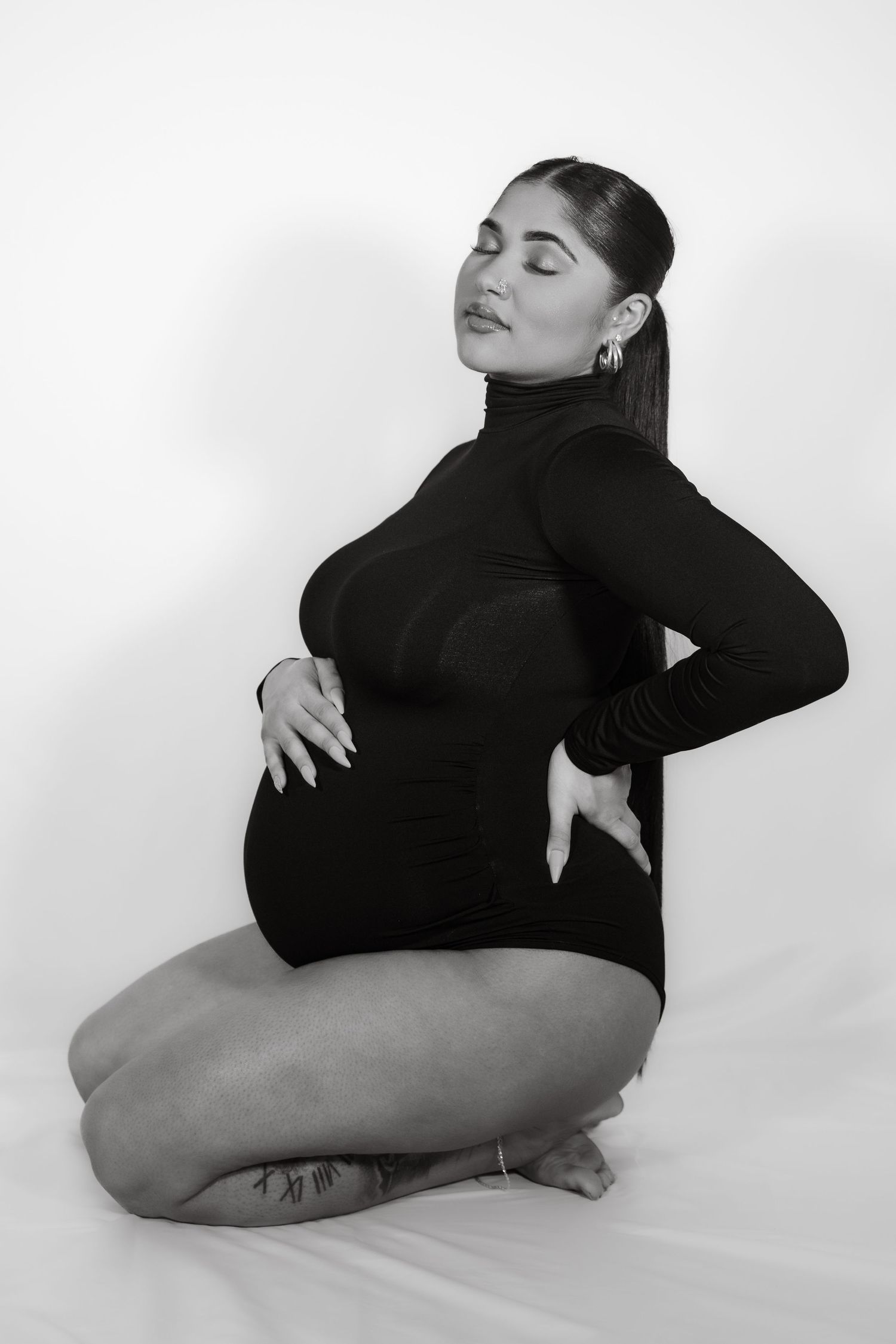 A monochrome maternity portrait showing an expectant mother in a black turtleneck against white background.