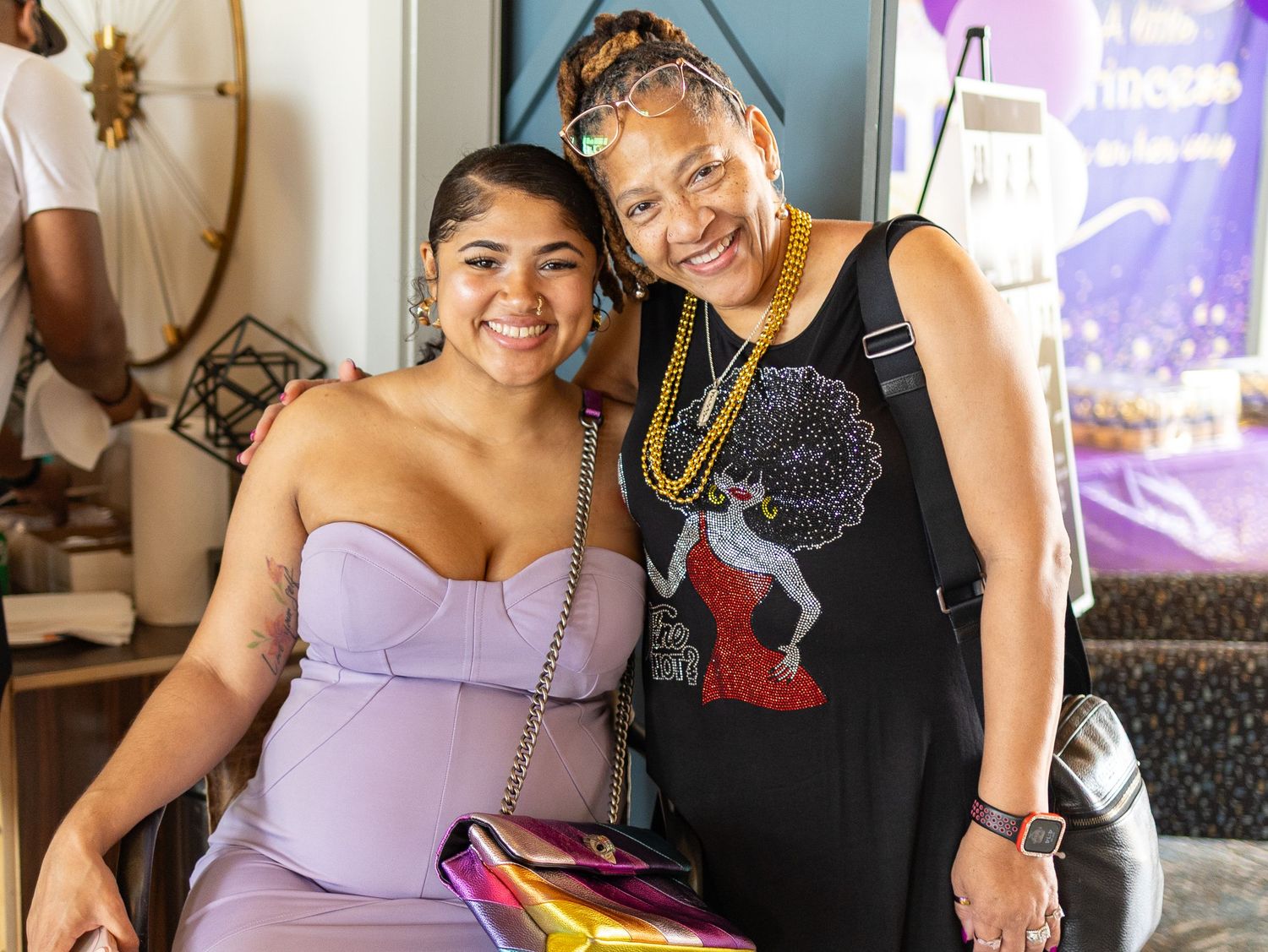 Two women smiling together at a celebration with festive decor in the background.