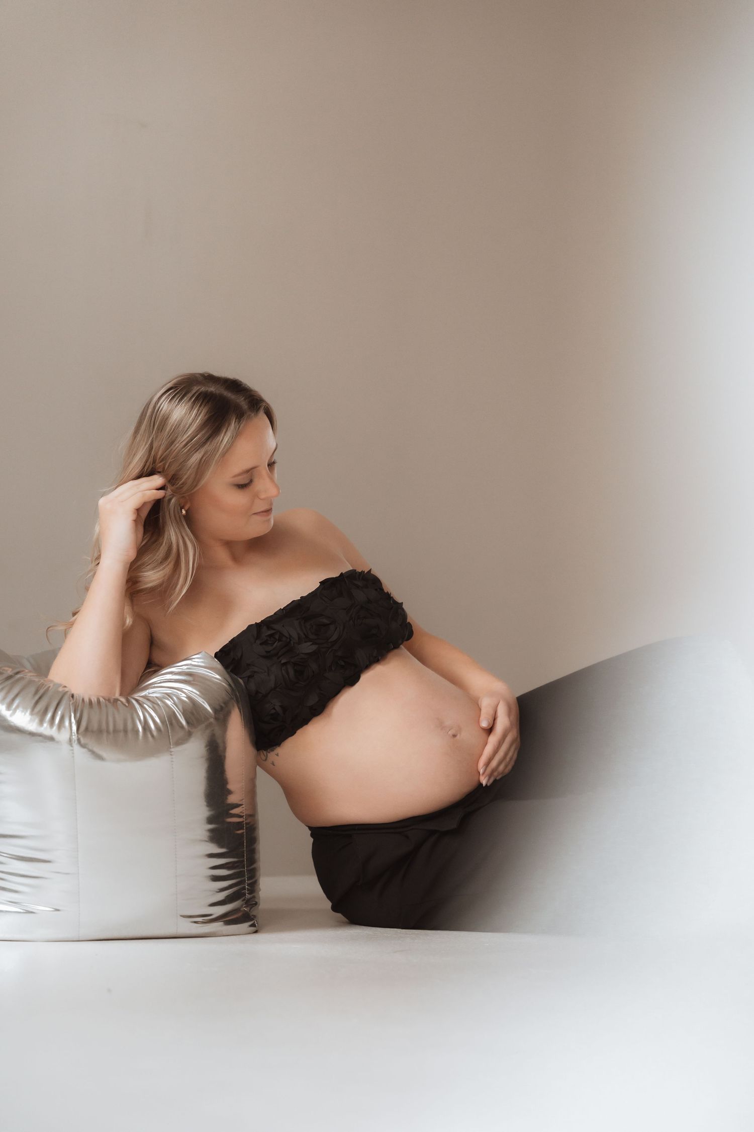Artistic maternity photos in black and white tones showing a pregnant figure reclining against neutral backgrounds.