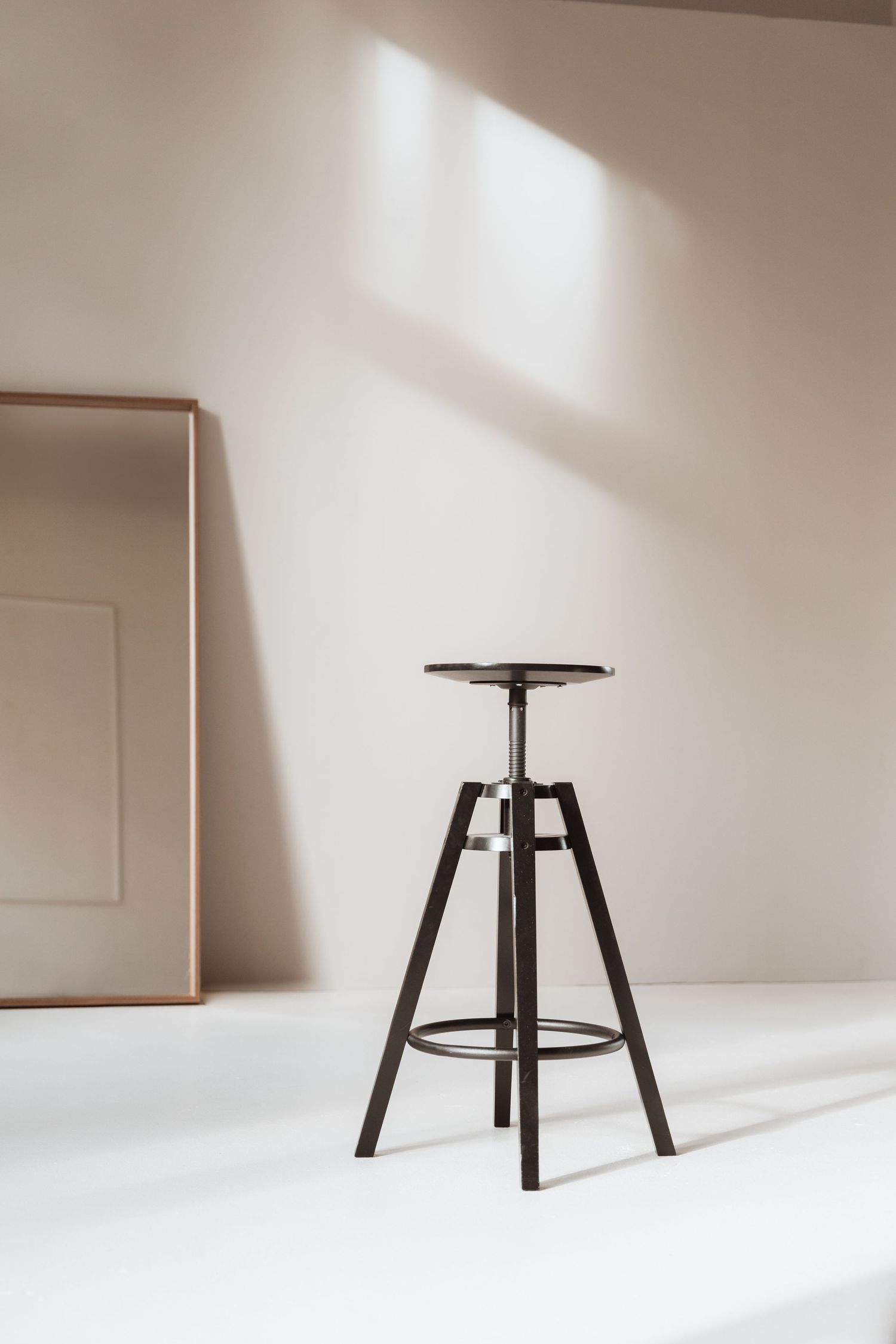 Minimalist black stool photographed in sequence against white wall showing assembly stages and dramatic shadows.