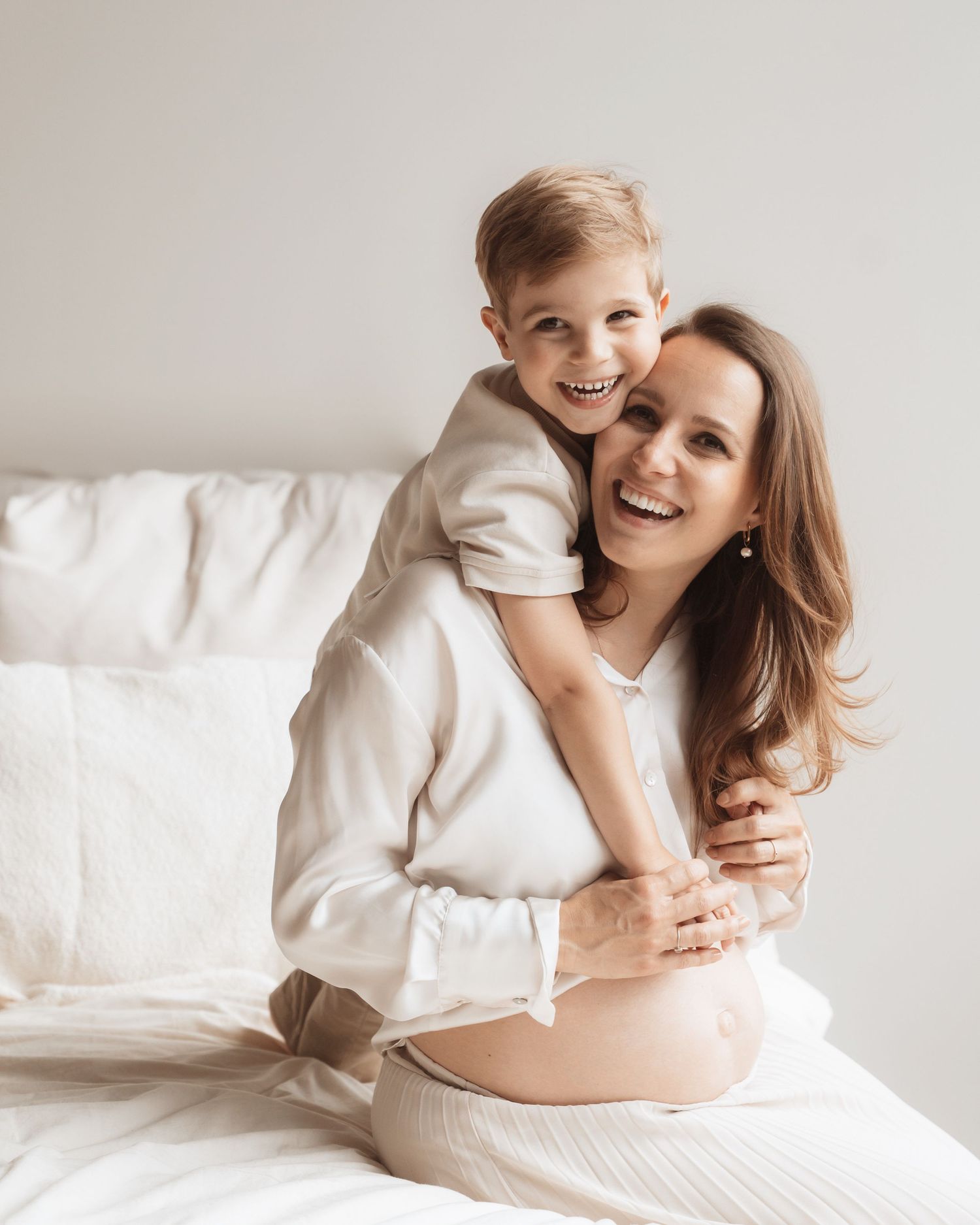 A tender moment captured in white as a mother and child share loving embraces on a bright bed.