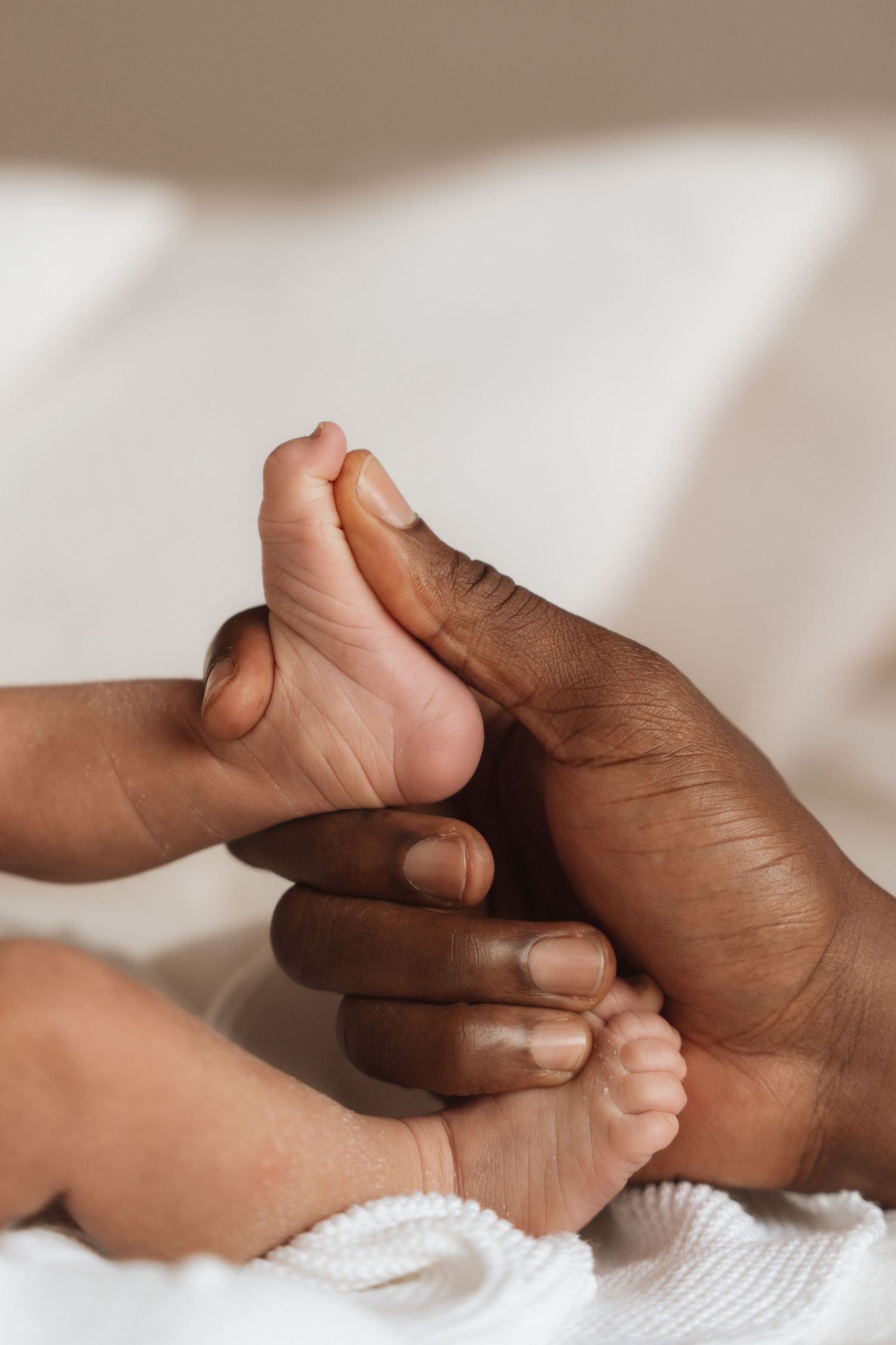 Adult hands gently holding tiny newborn baby feet on a white blanket, showcasing tender parent-child bond.