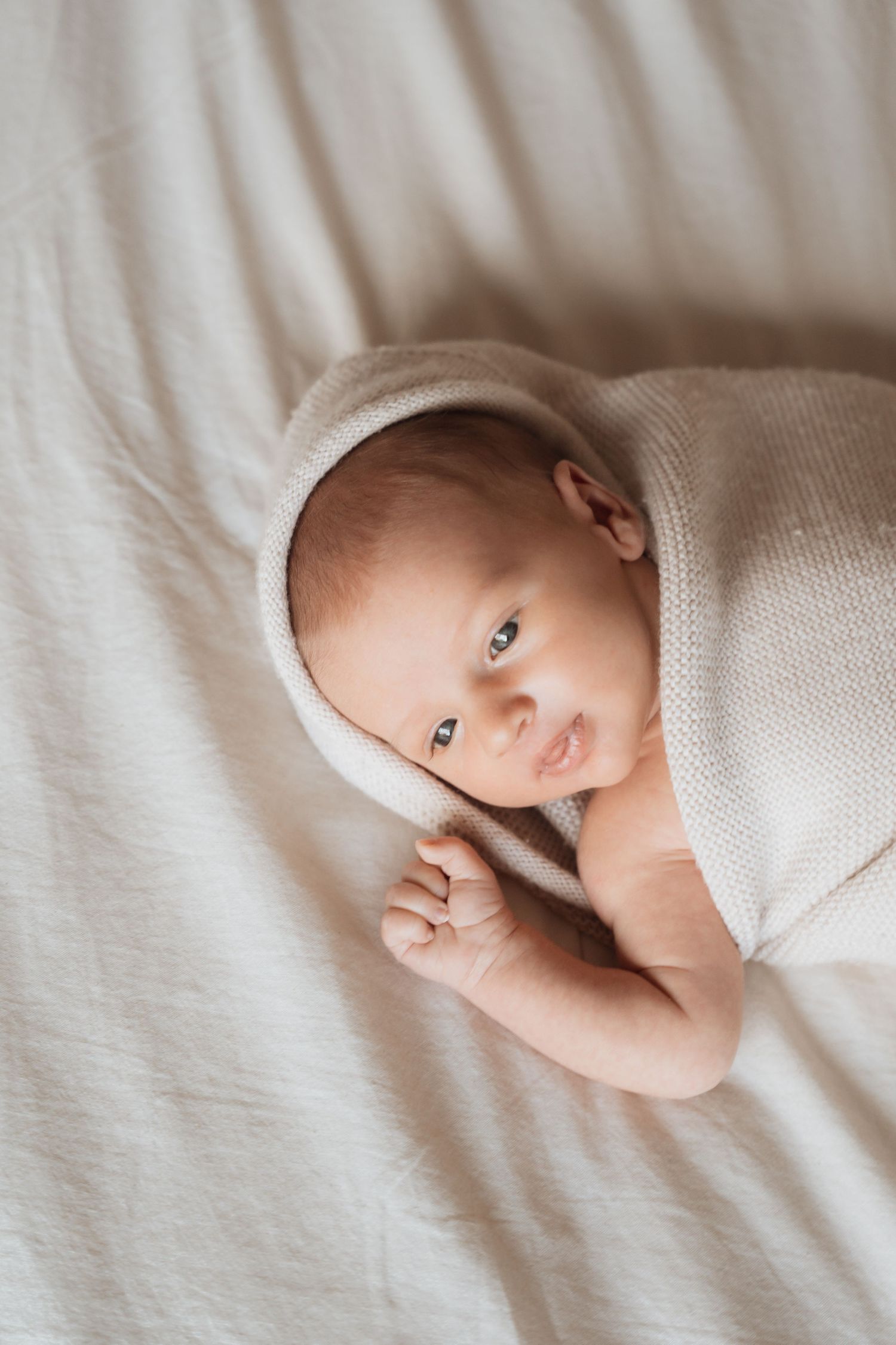 Sleeping newborn wrapped in cream colored blanket on white bedding.
