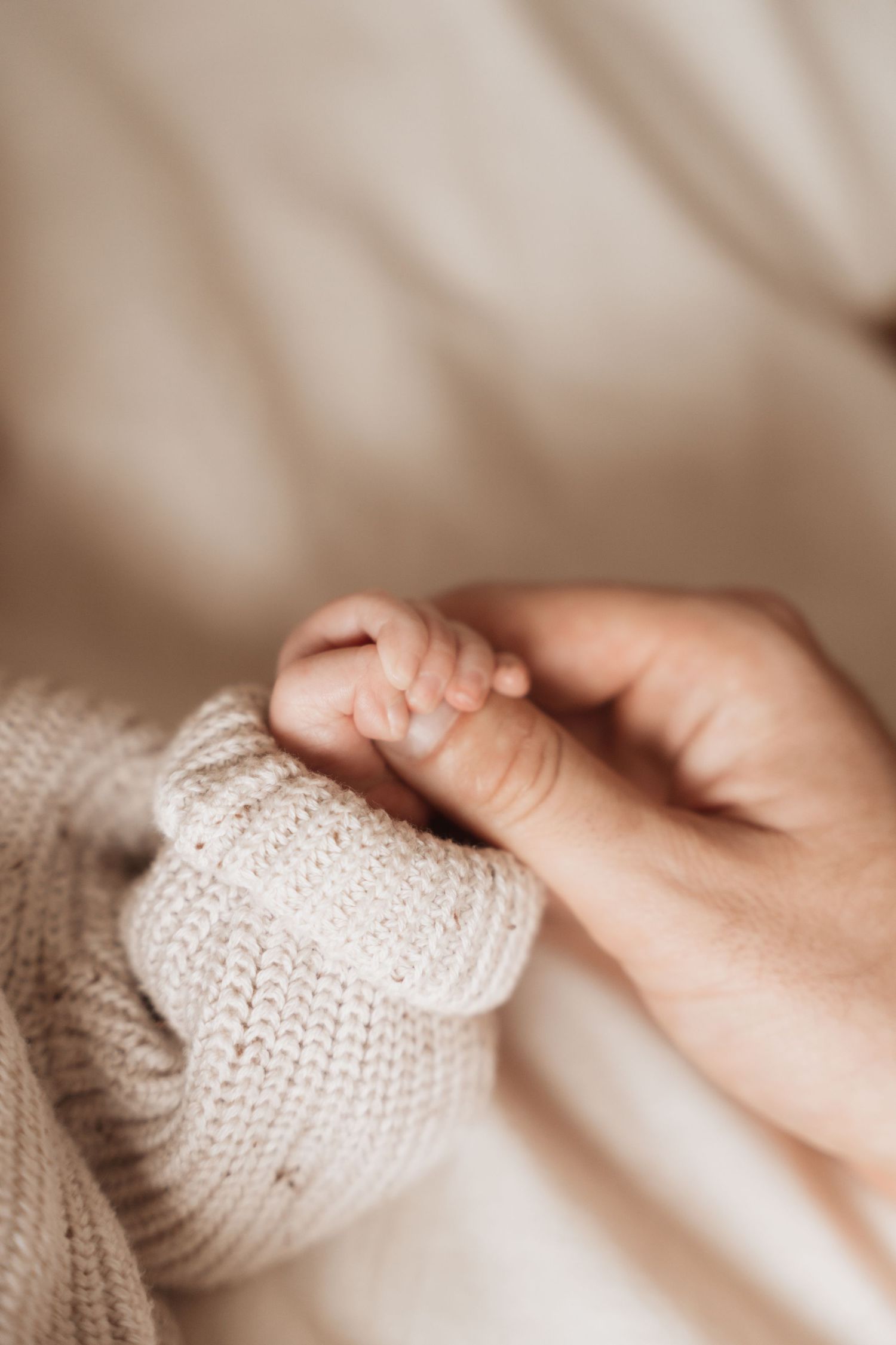 Close-up of tiny hand grasping adult finger through soft knit fabric.