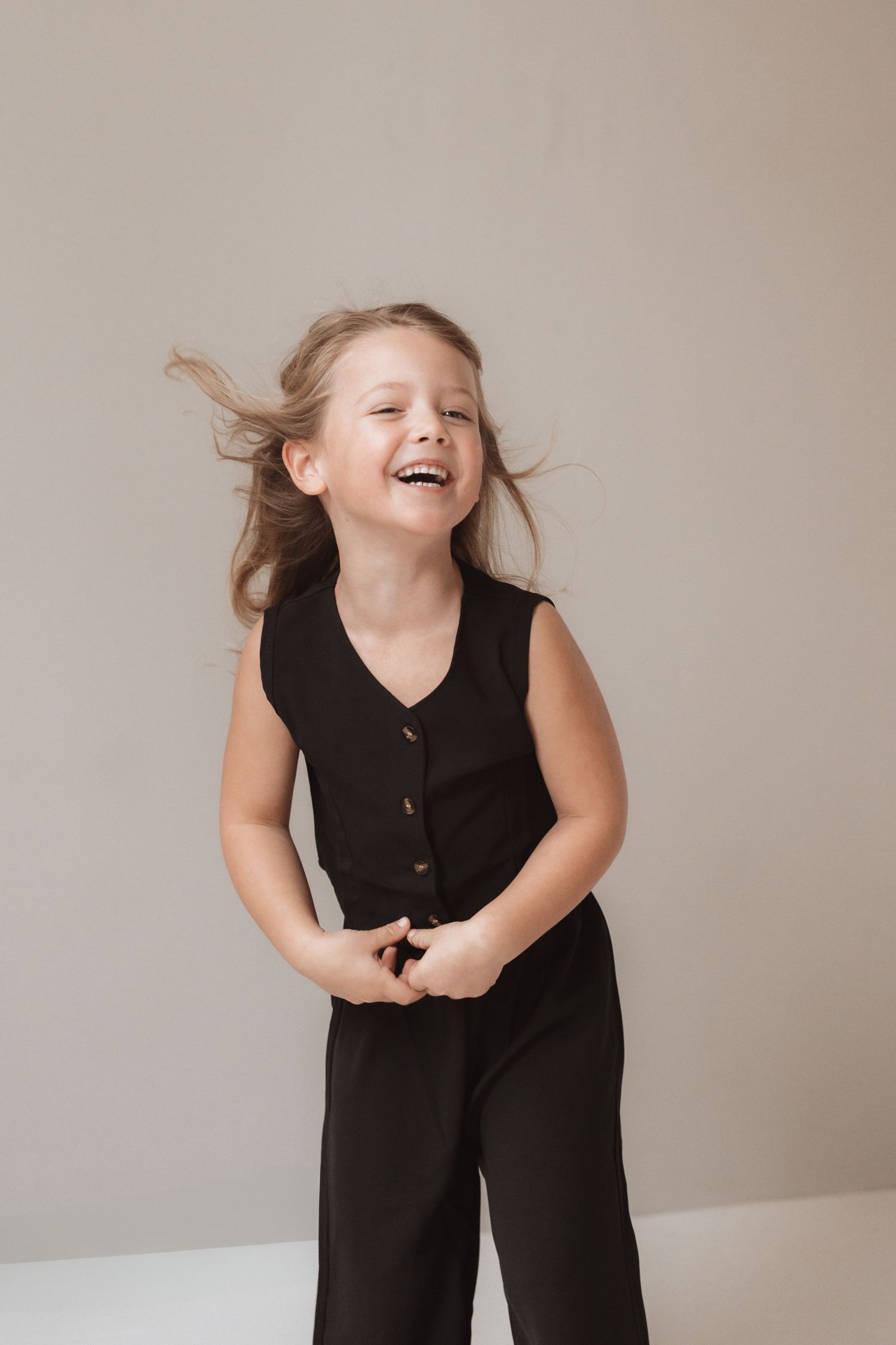 A series of playful poses in a black sleeveless jumpsuit against a neutral background.