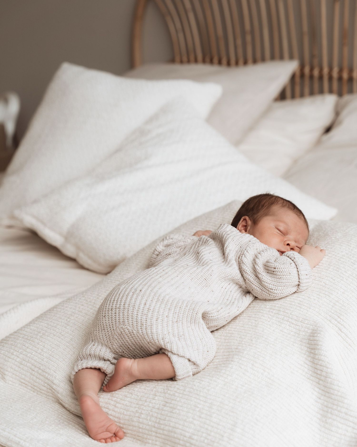 Baby sleeping on white textured bedding in a minimalist setting.