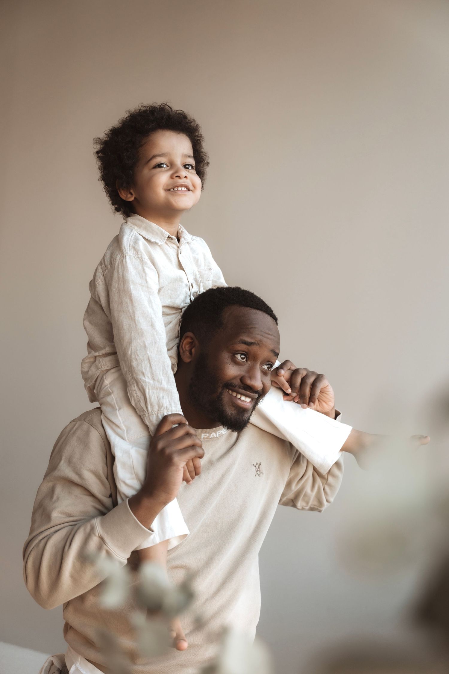 Joyful parent and child playing and laughing in matching beige outfits.