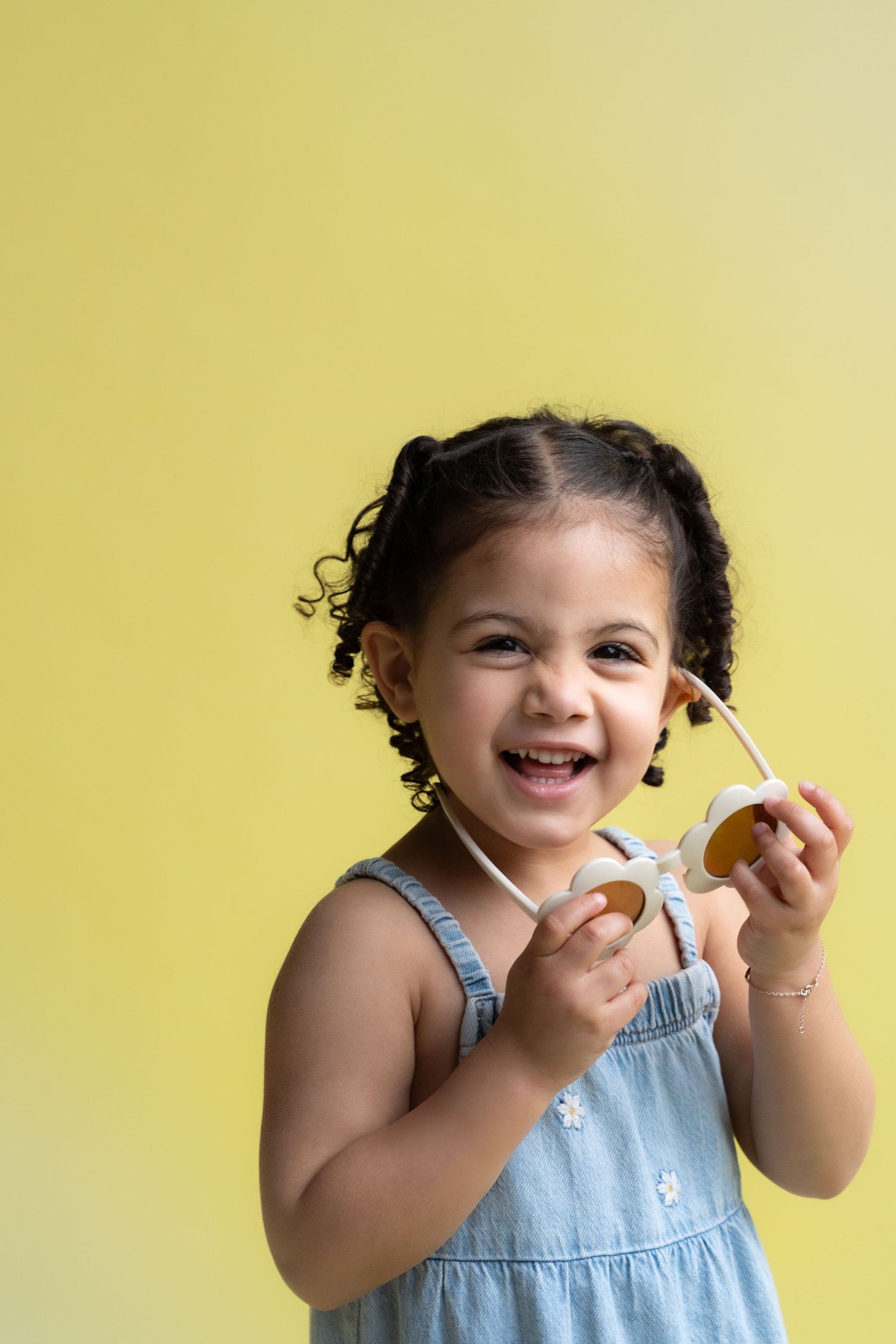 A child in denim overalls laughs joyfully while playing against a yellow background.