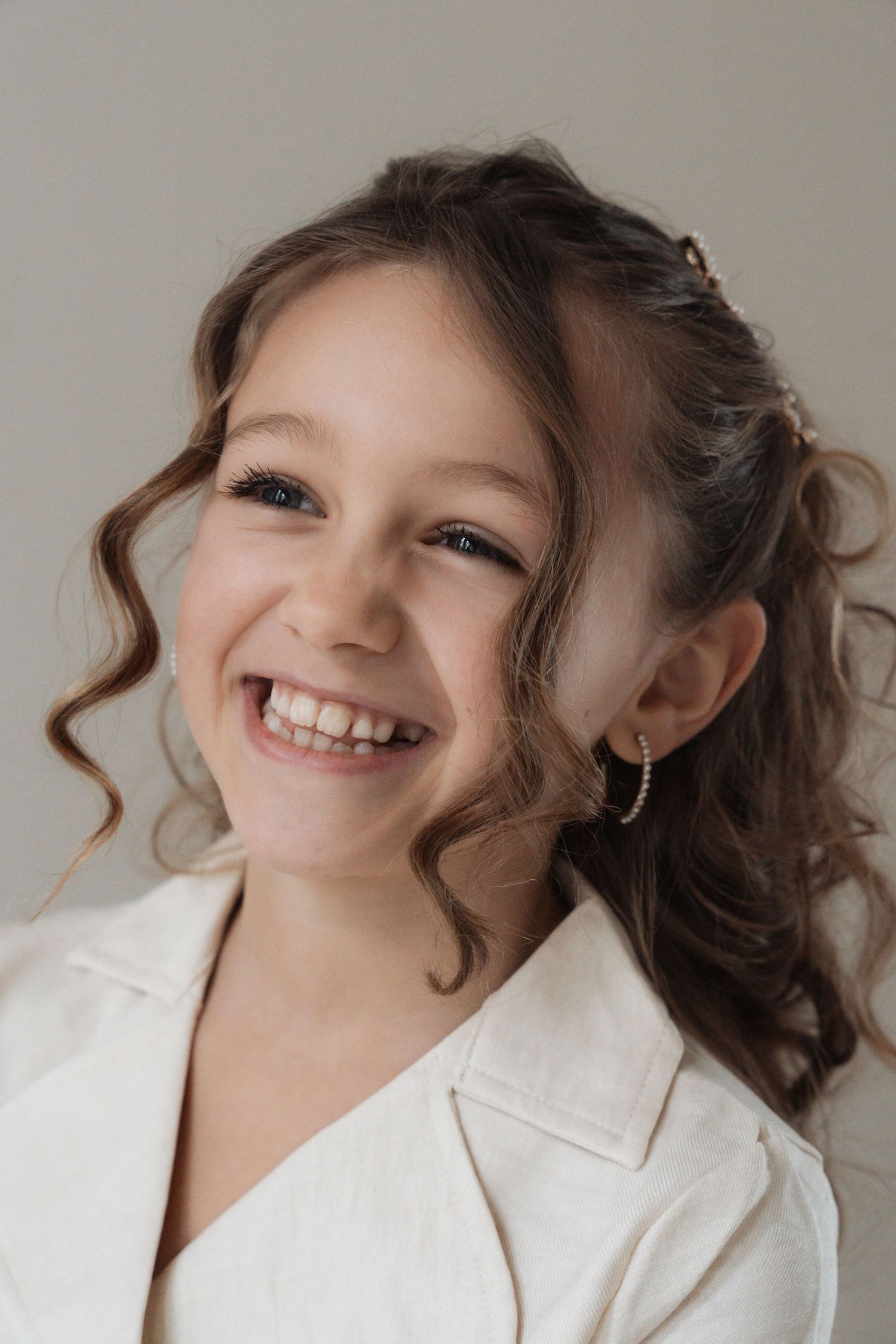 A series of five headshots showing a person in a white blazer with curly brown hair expressing joyful smiles.