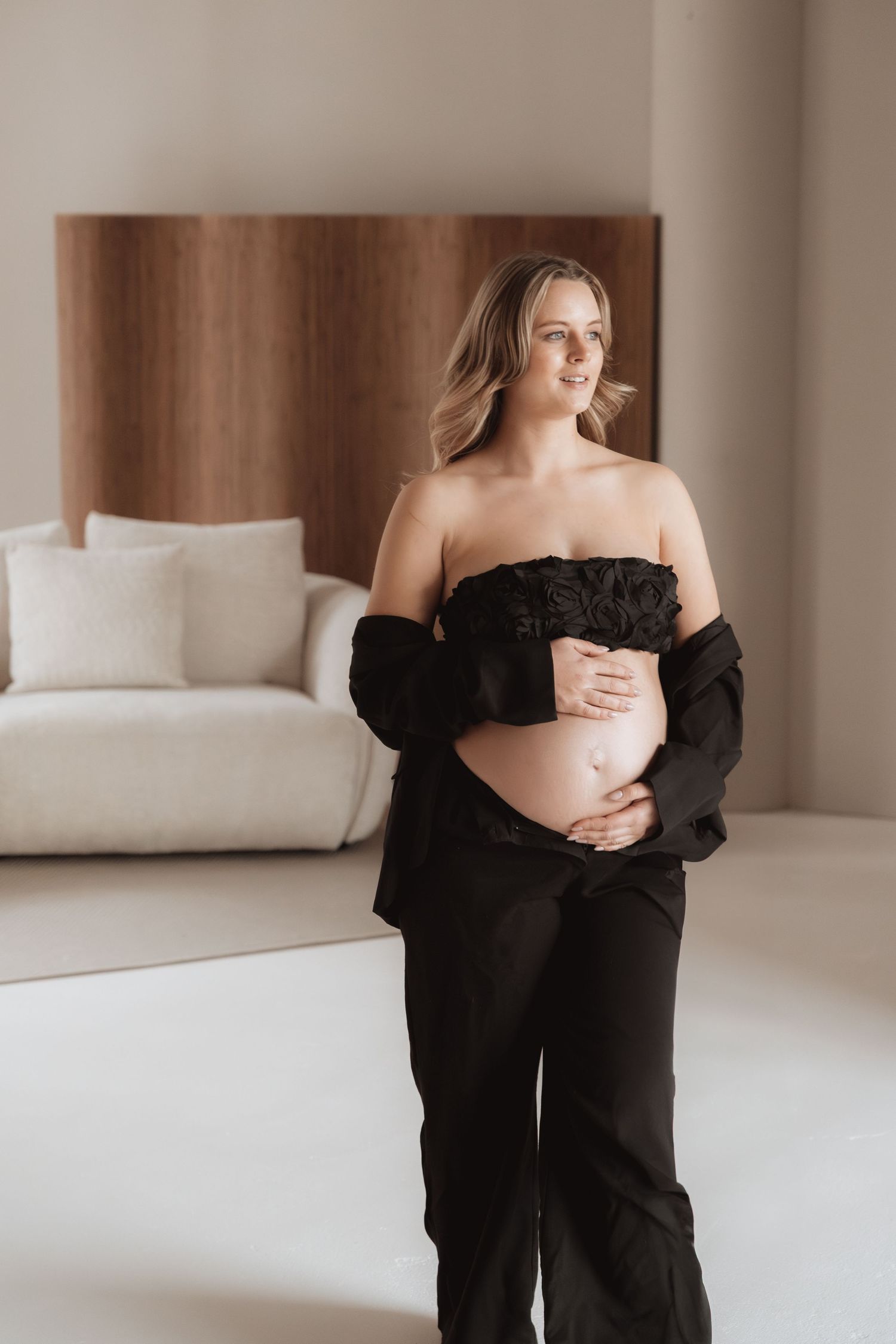 Minimalist maternity portraits featuring a woman in black sweater against neutral wall and bedding.