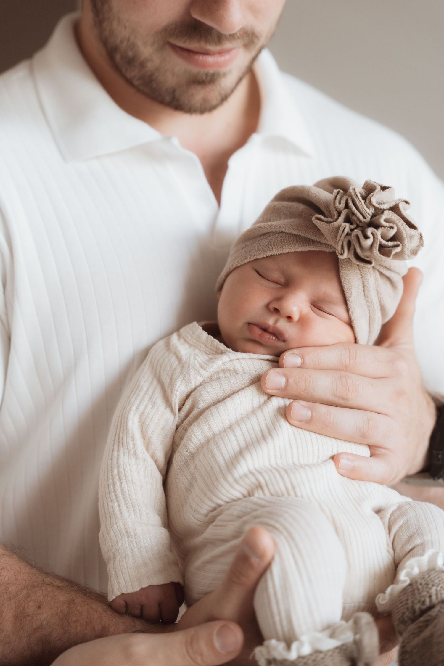 Newborn baby in cream outfit being gently cradled in parent's arms.