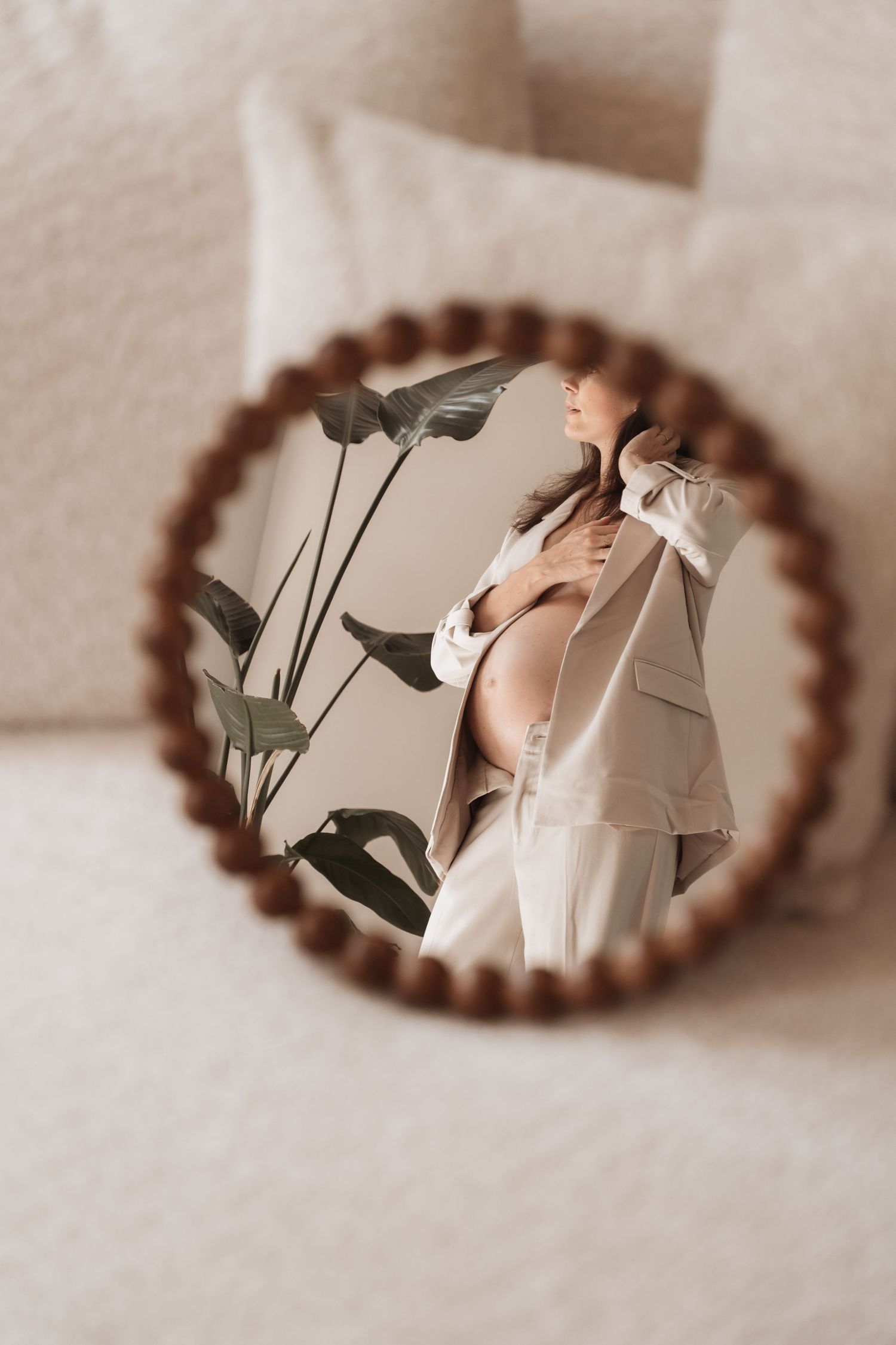 Artistic reflection of pregnant belly in round wooden mirror with plant shadows.