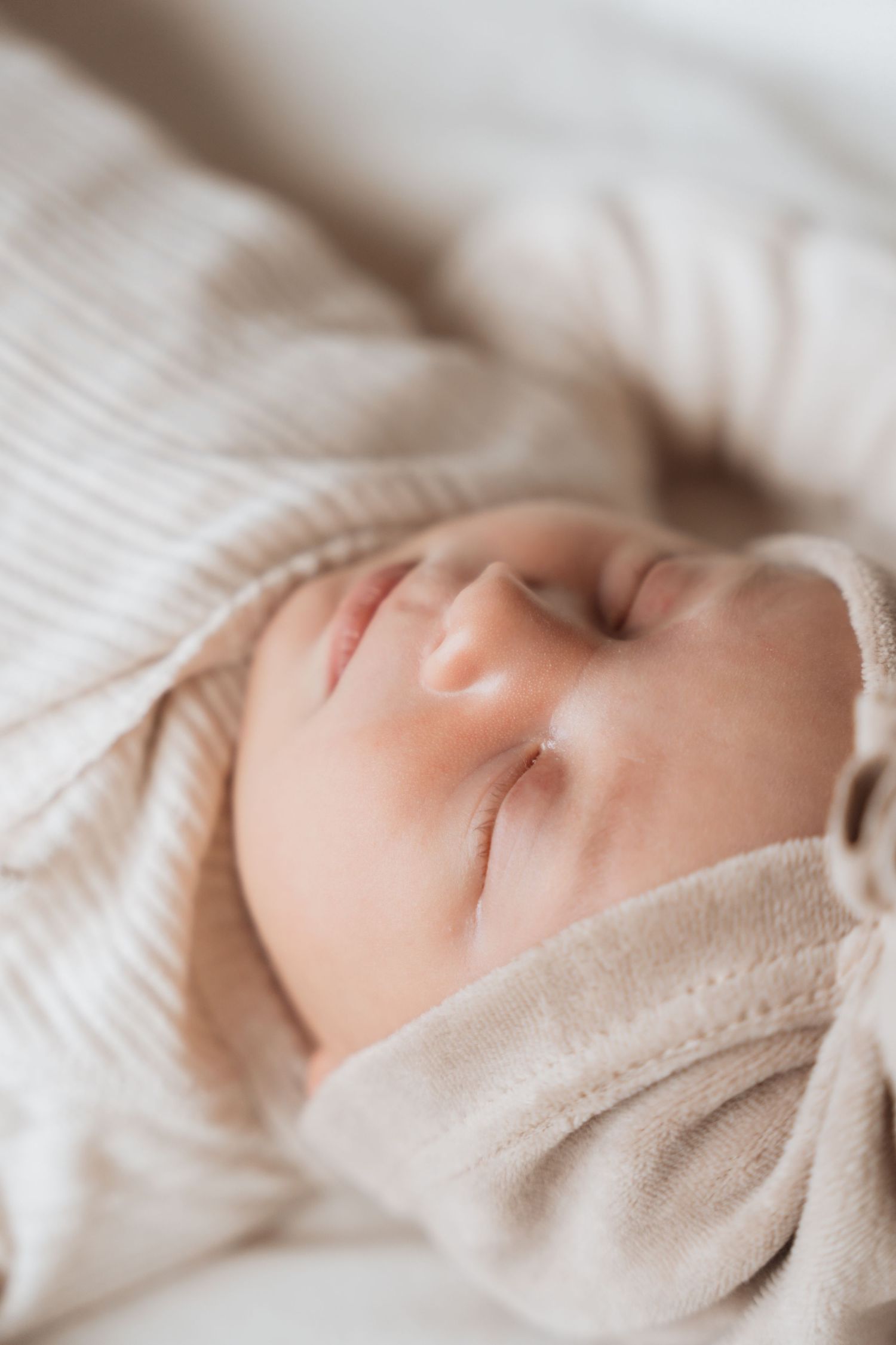 Peaceful sleeping baby in soft beige clothing against white textured bedding.