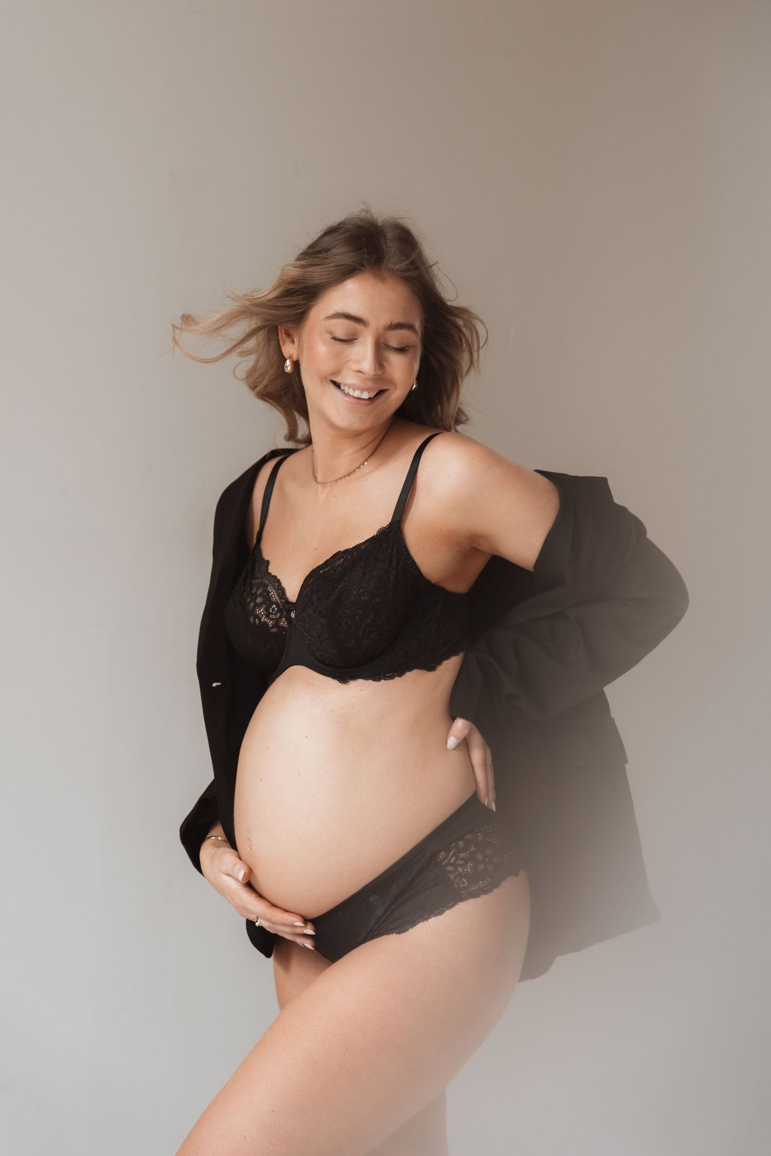 Maternity photo series showing a woman in black lingerie against a gray backdrop in artistic poses.