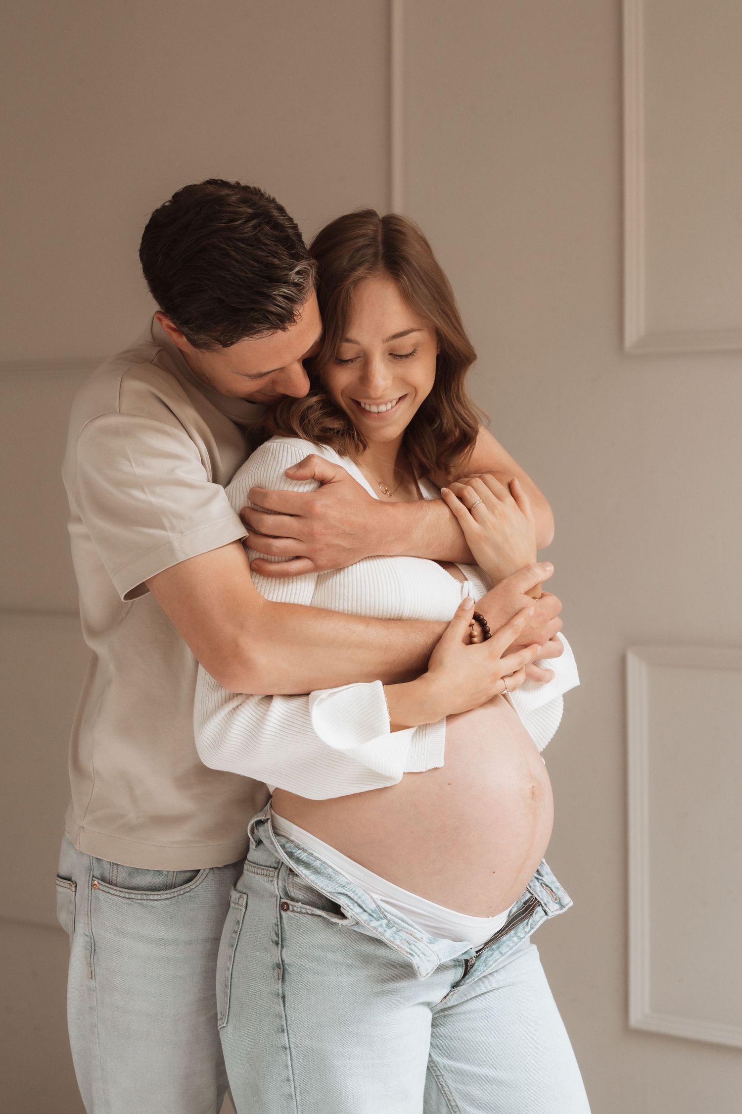 Romantic maternity portrait of couple embracing in casual denim and white.