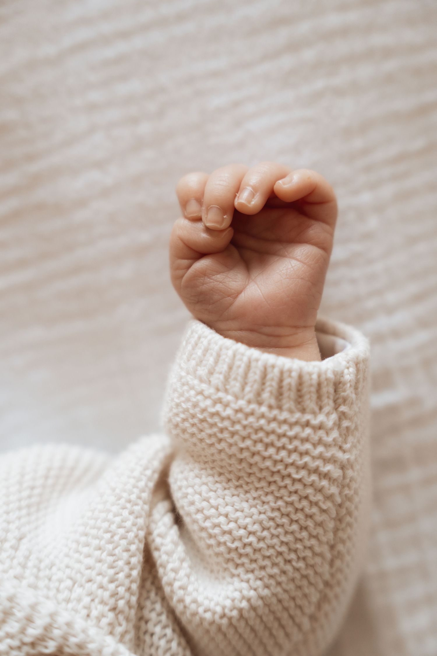 Close-up of tiny hand against cream knitted sweater texture.
