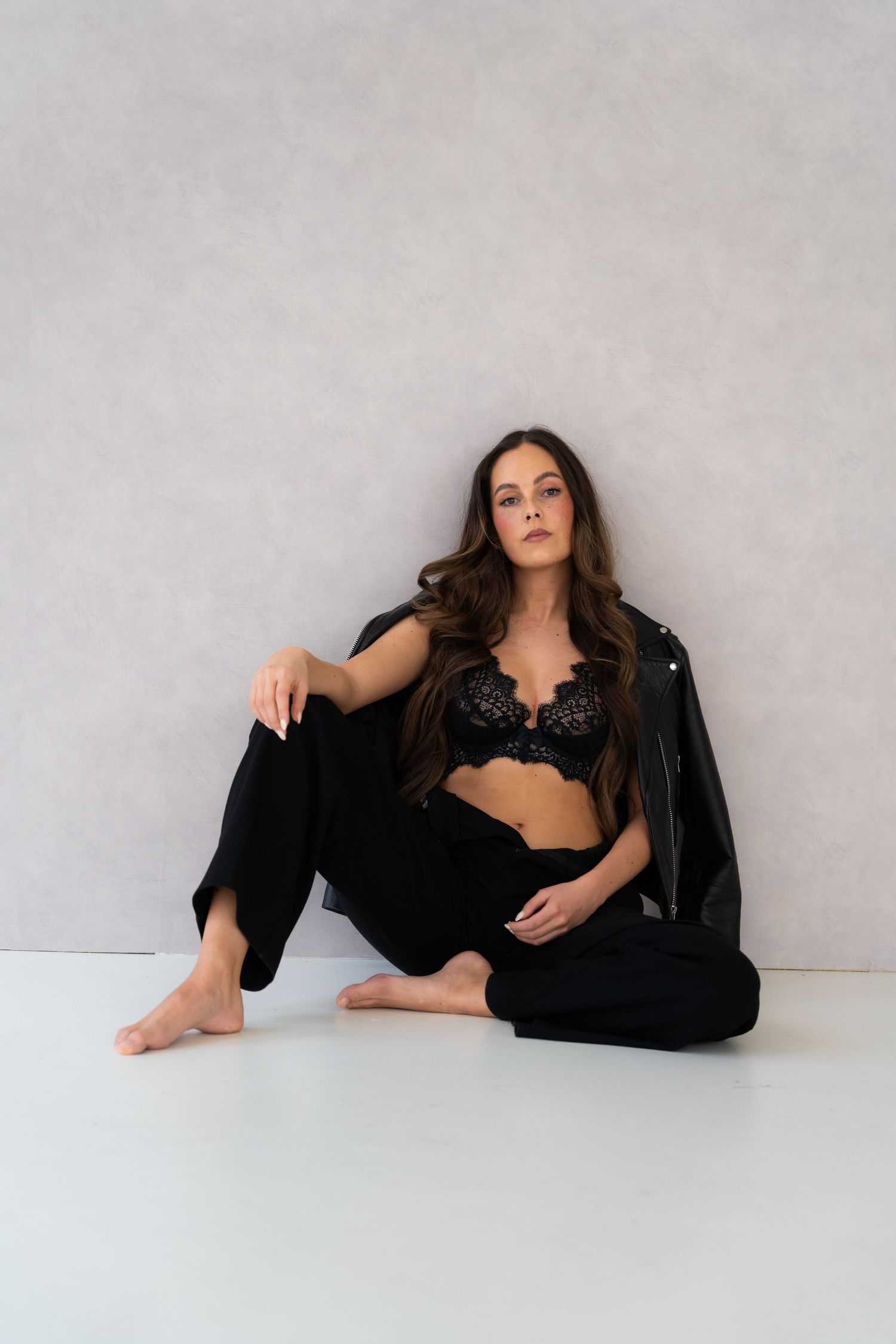 Model in black outfit reclining on white floor in artistic poses.