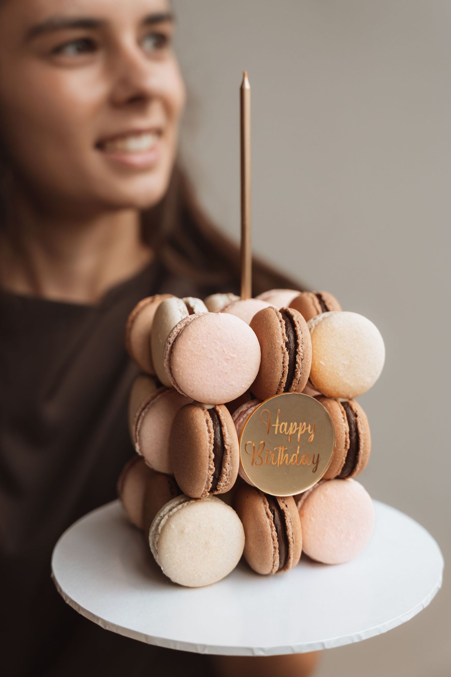 Woman holding a birthday cake made of stacked macarons with a candle and Happy Birthday gold topper.