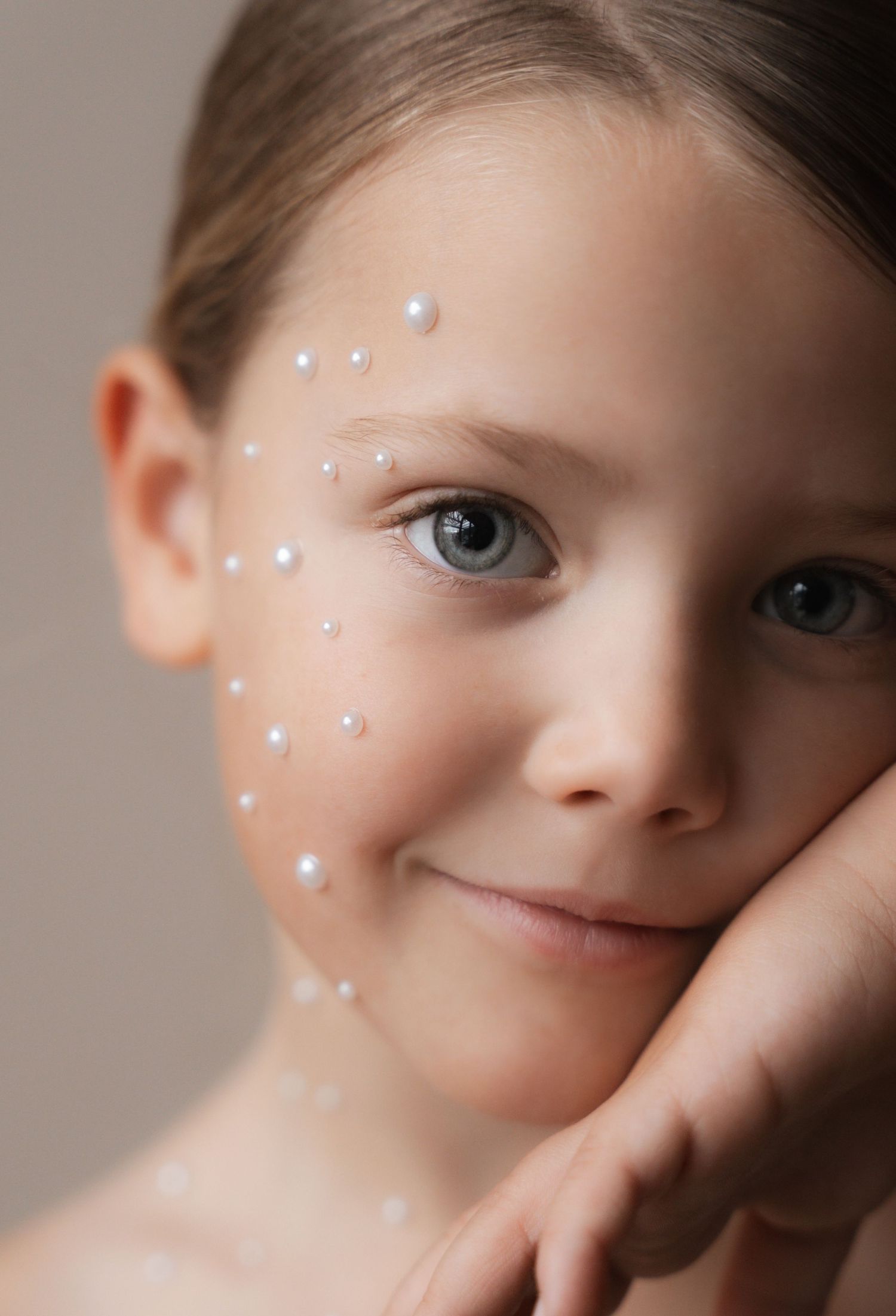Young girl with pearl decorations on her face, smiling softly with blue-gray eyes and a gentle expression.