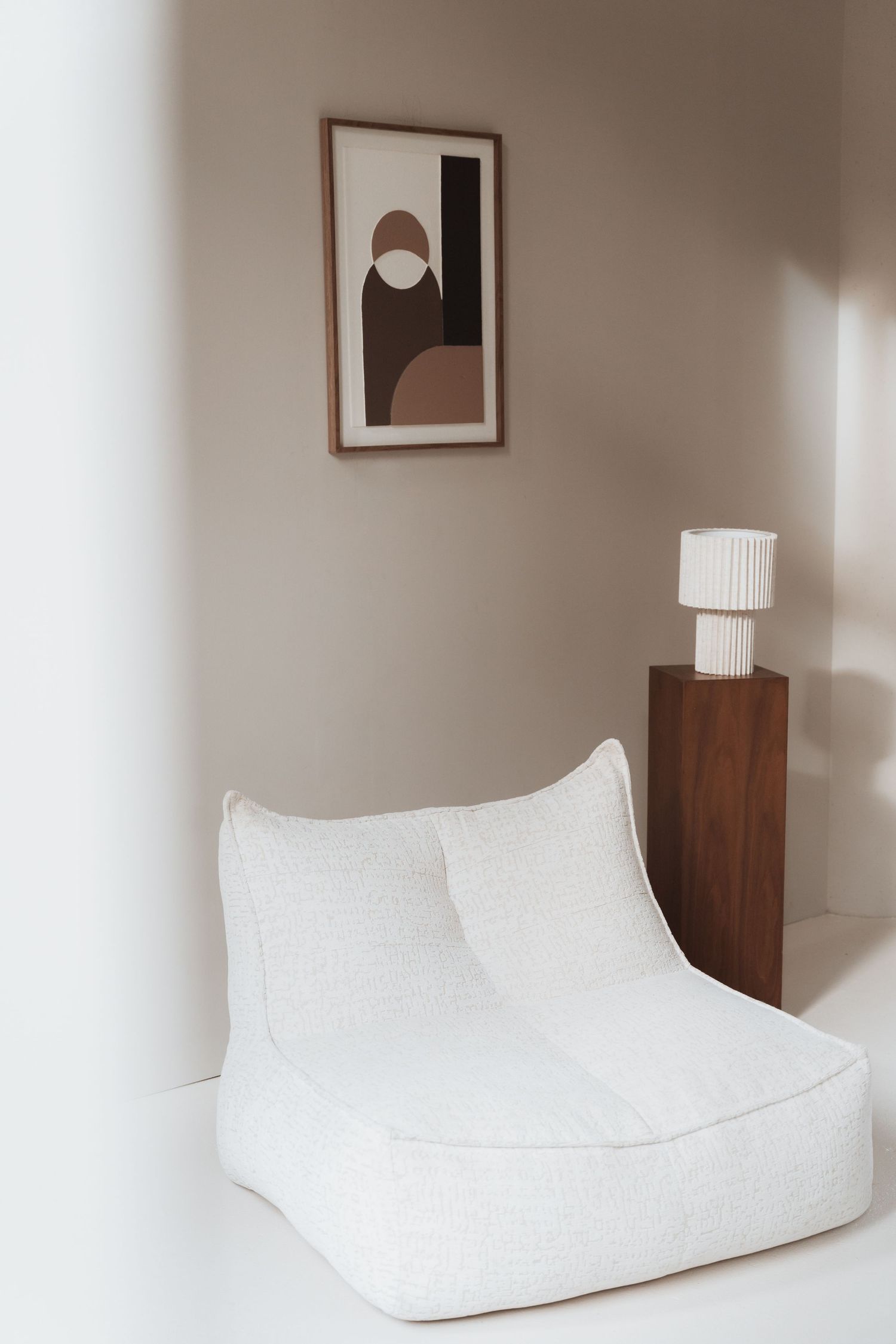 Modern minimalist bedroom interior with white cushioned seating and wooden furniture against neutral walls.