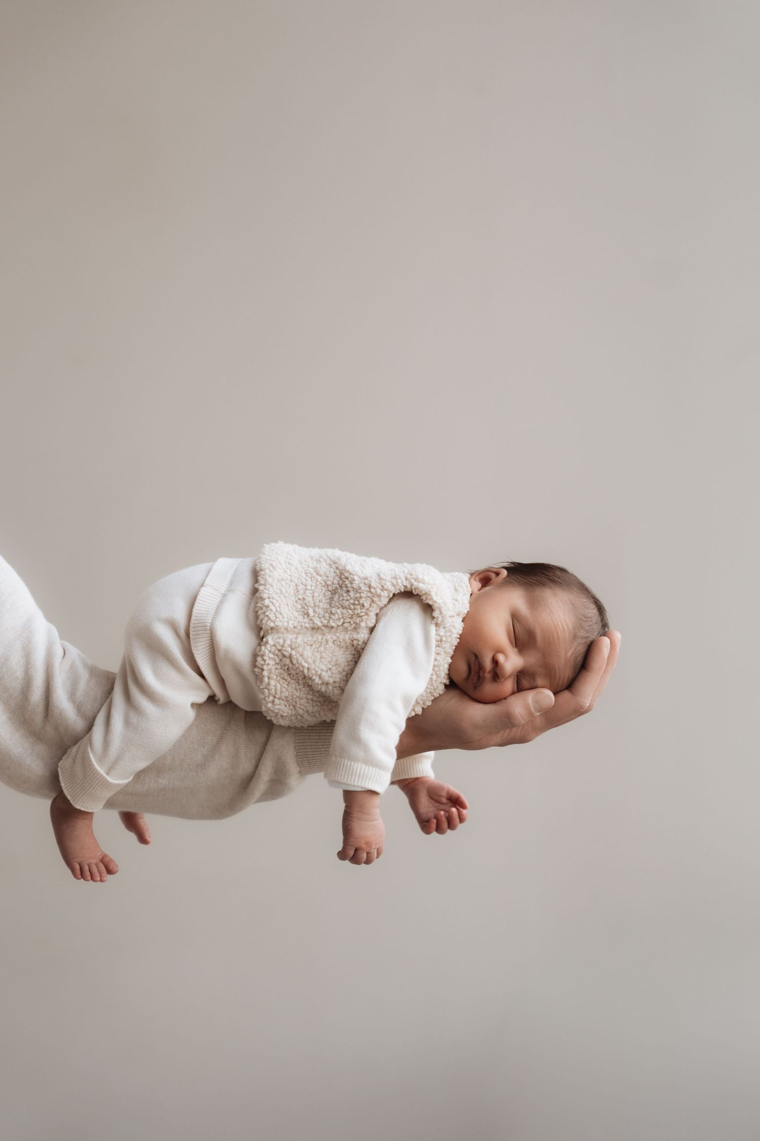 A sleeping baby in white clothing appears to float against a light gray background in a creative composite photo.