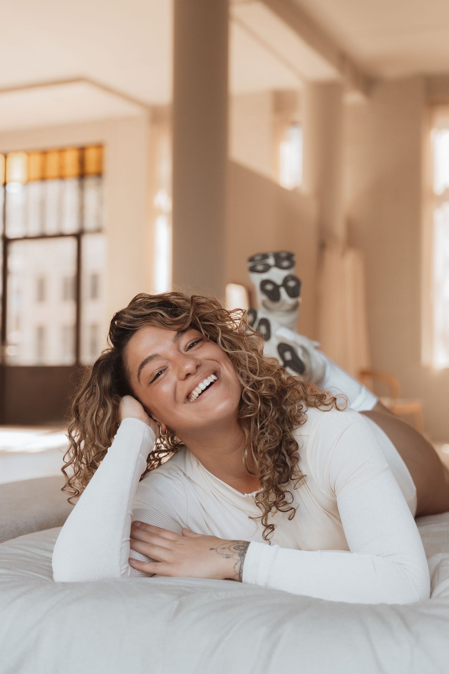 Person in white sweater relaxes on bed with joyful expressions.