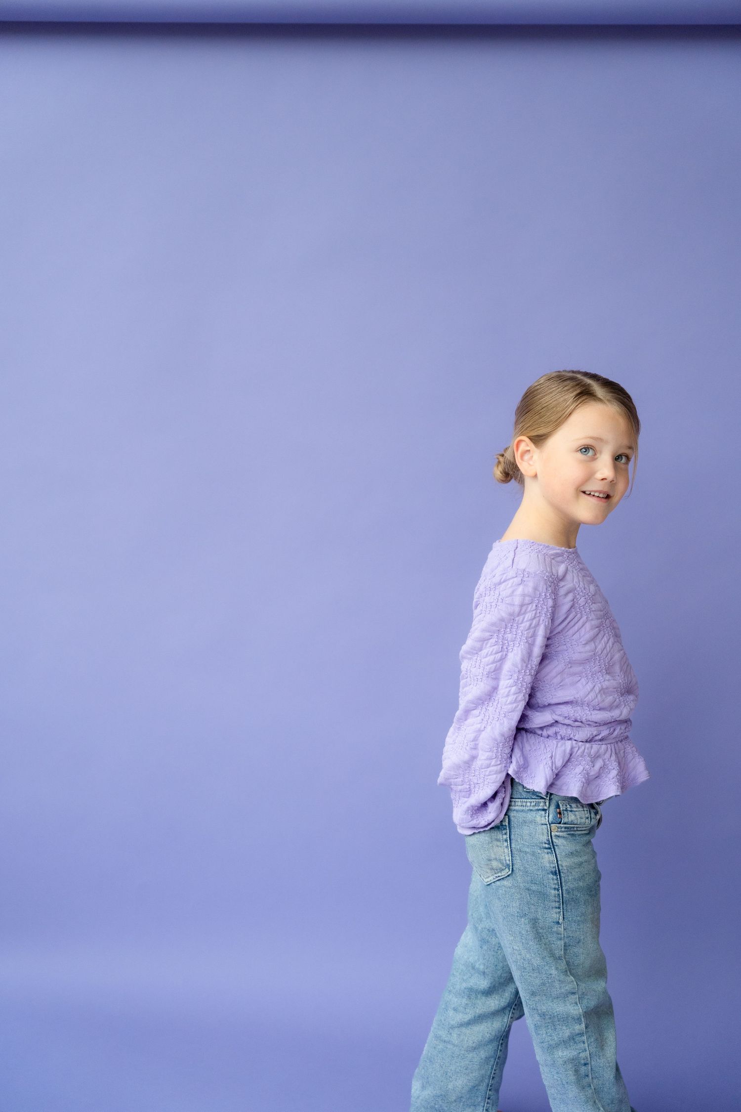 A figure in a lilac ruffle top and light blue jeans poses against a purple backdrop in a sequence of photos.