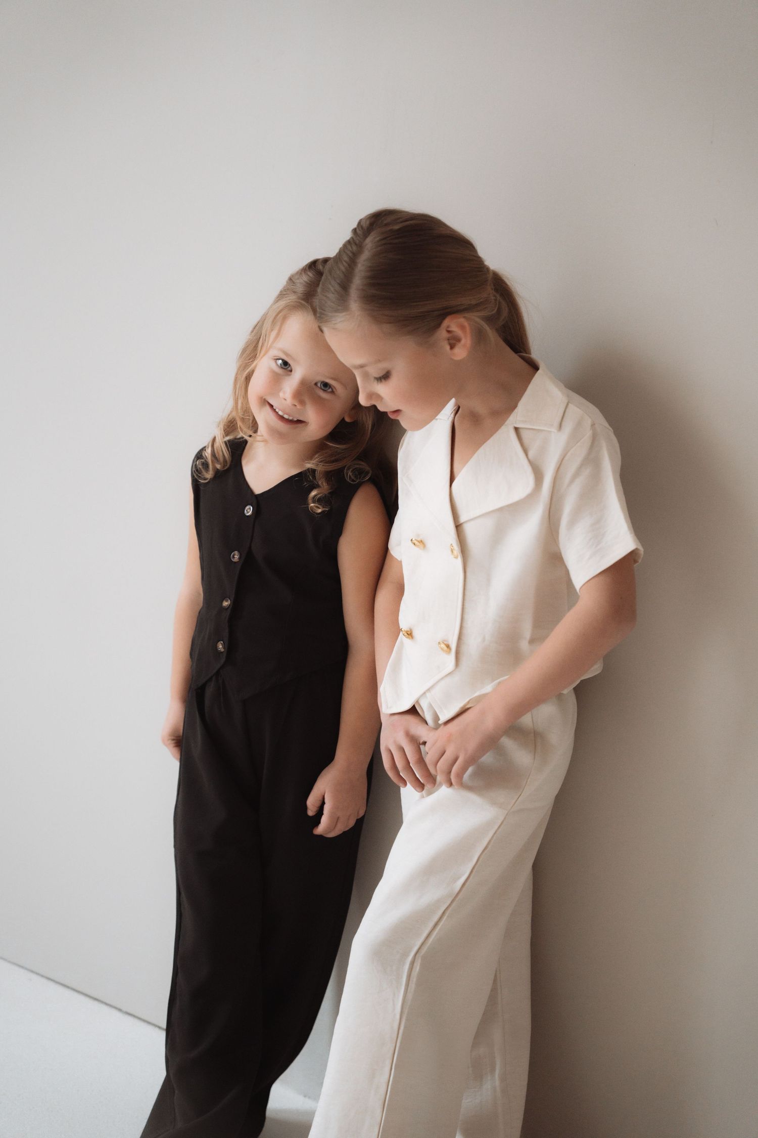 Two figures in contrasting black and white dresses lean against a light colored wall creating an artistic composition.